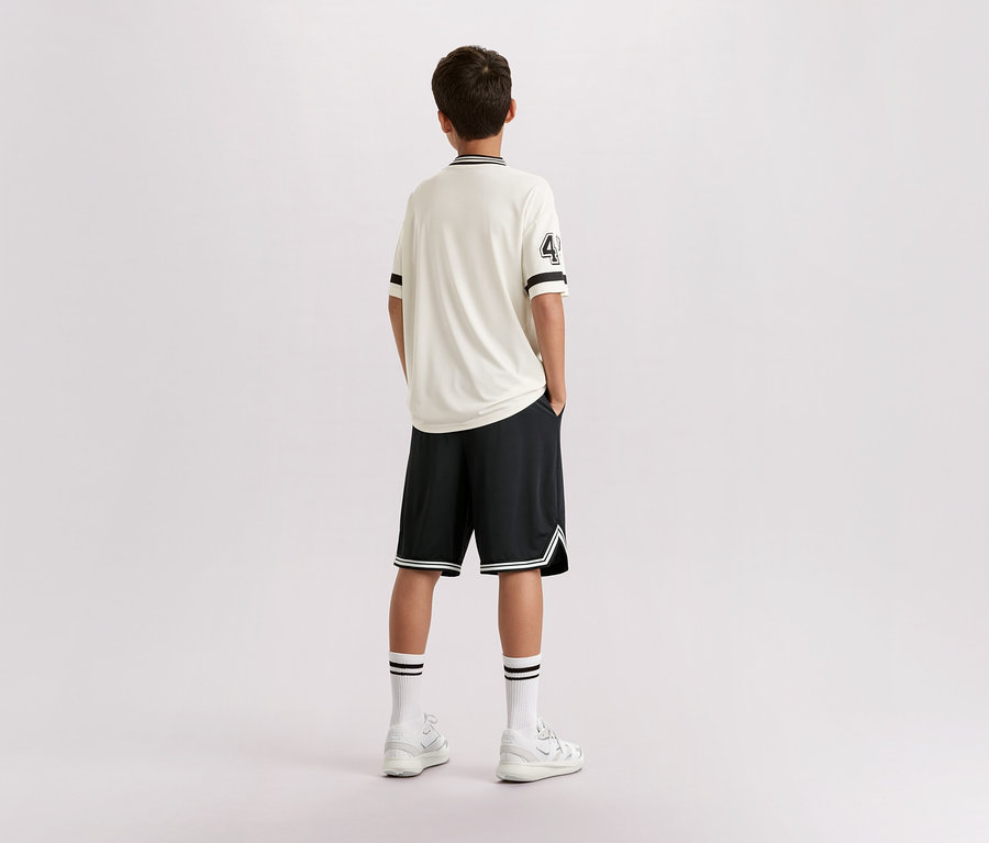 Egy fiatalember áll háttal a kamerának, világos pólót visel 4-es számmal, fekete rövidnadrágot, fehér zoknit és tornacipőt.