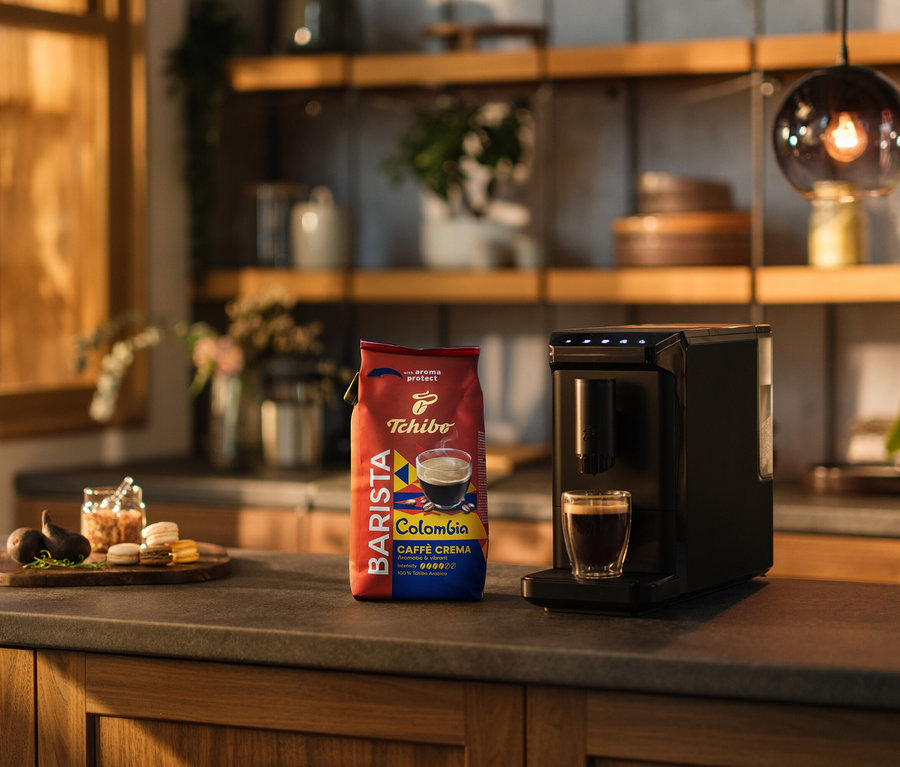 A konyhapulton kávéfőző, egy csésze kávé és egy csomag BARISTA Origins Colombia – 1 kg szemes kávé látható.