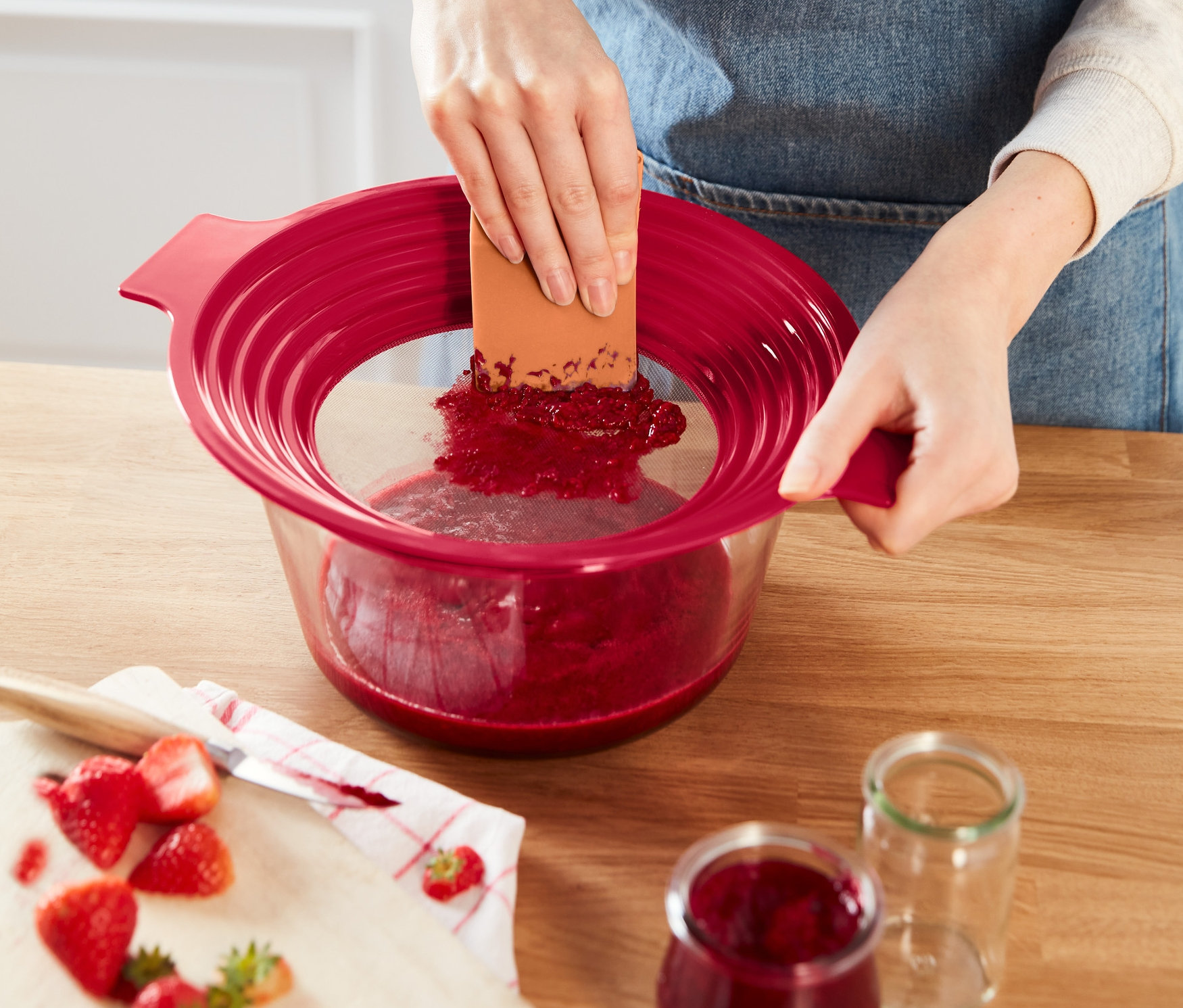 Nő epret passzíroz egy piros 2 az 1-ben lisztszitán és passzírozón keresztül.