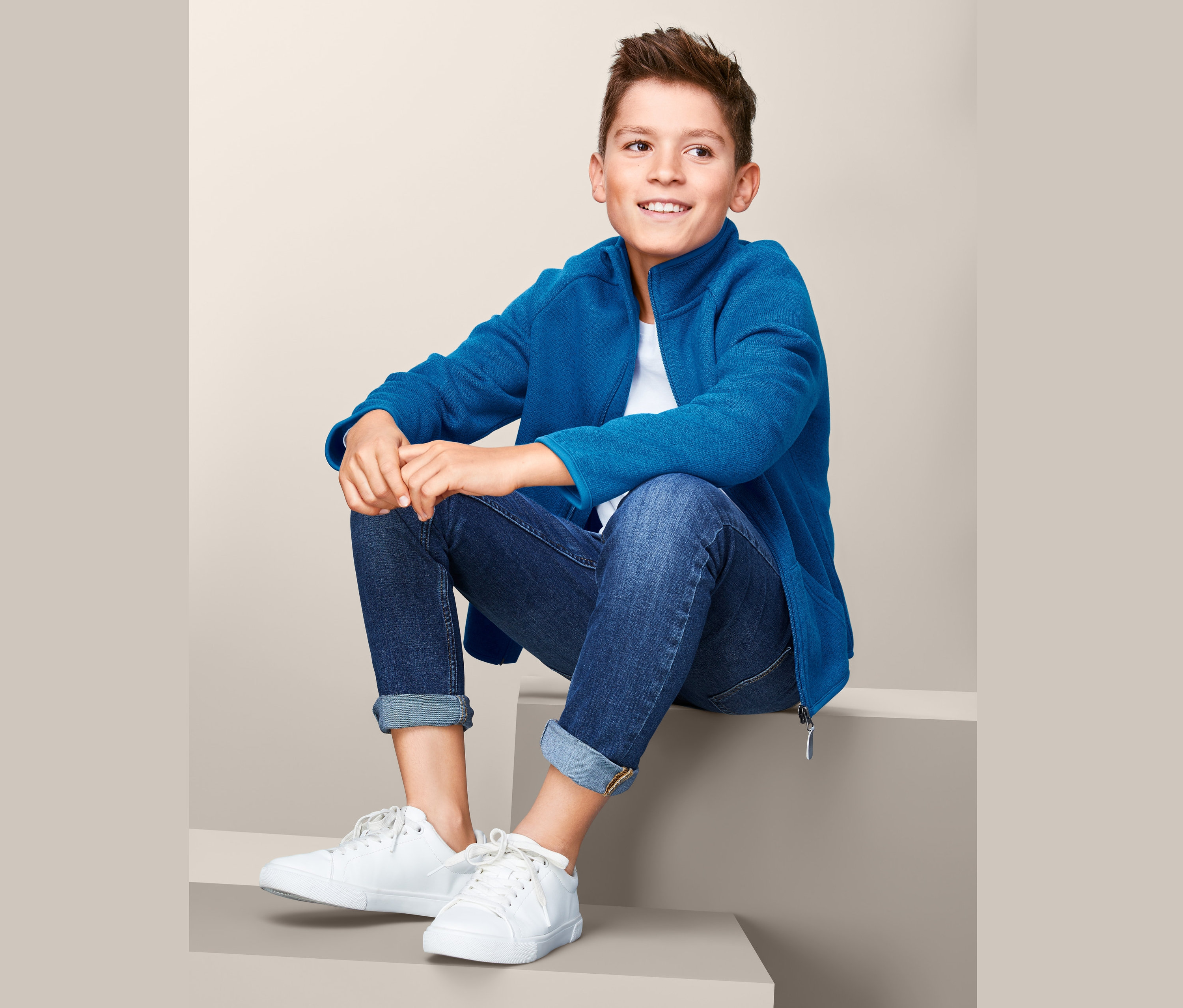 Fiú ül a lépcsőn, kék kötött polárfelsőt visel.