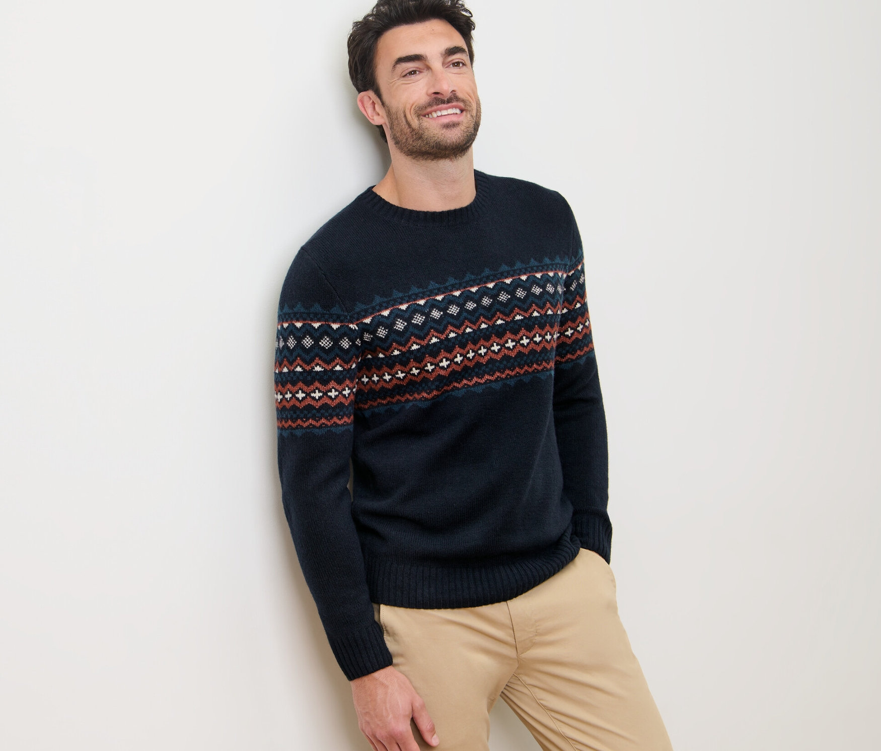 Férfi a falnak támaszkodva, norvég mintás kötött pulóvert visel.