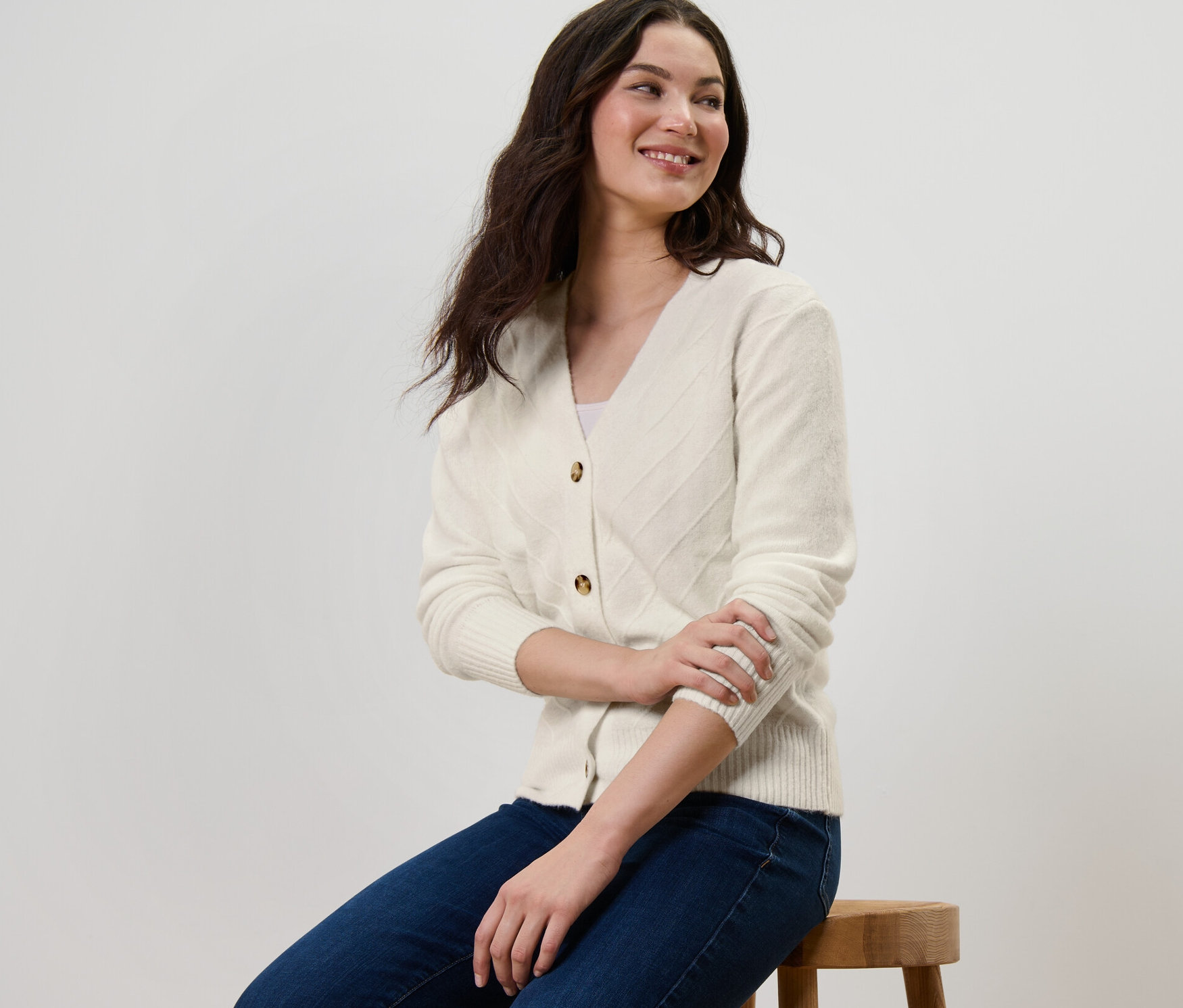 Egy nő ül egy széken, és kötött mintás, krémfehér kardigánt visel.