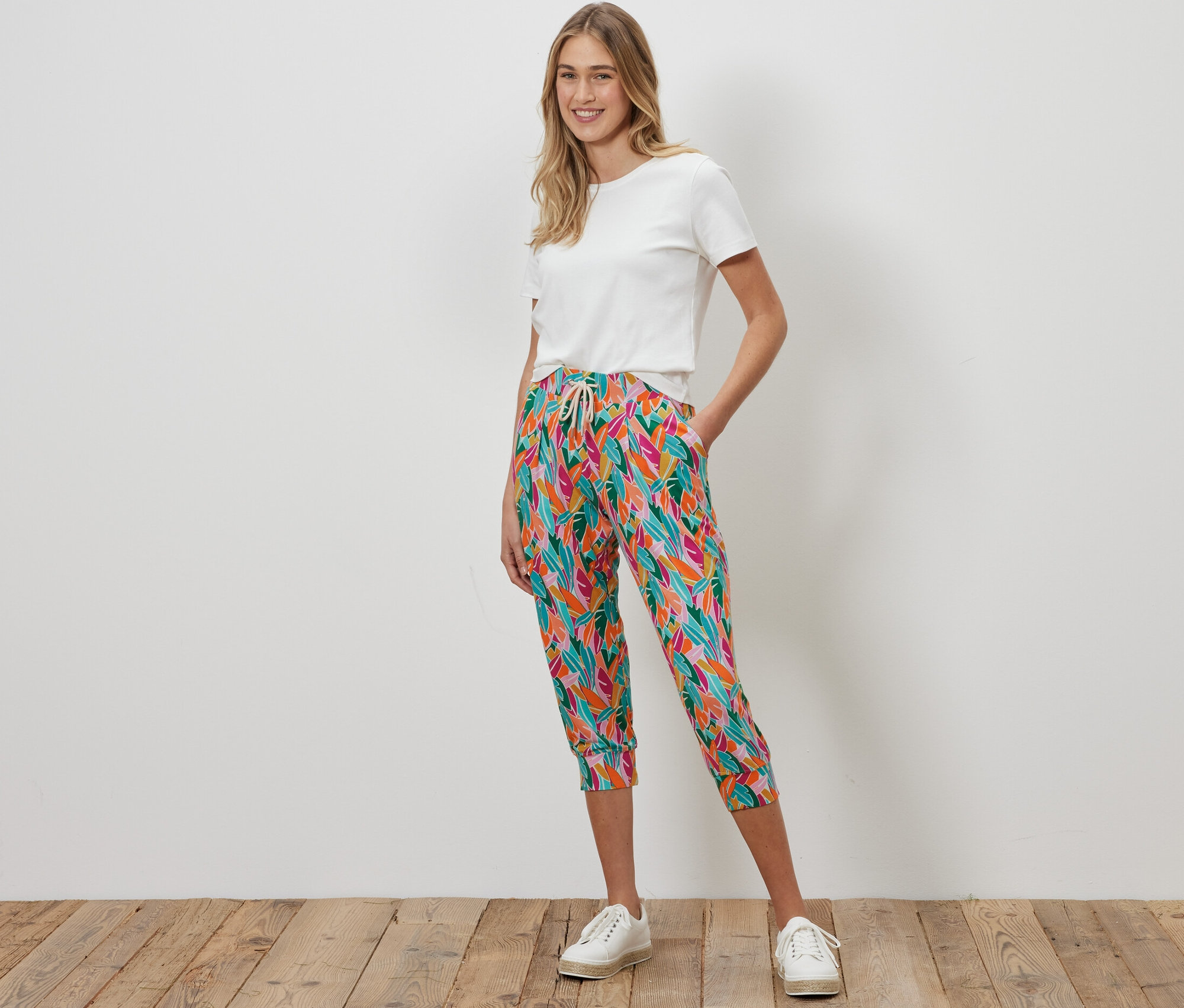 Egy nő áll, és színes 3/4-es jersey nadrágot és fehér pólót visel.