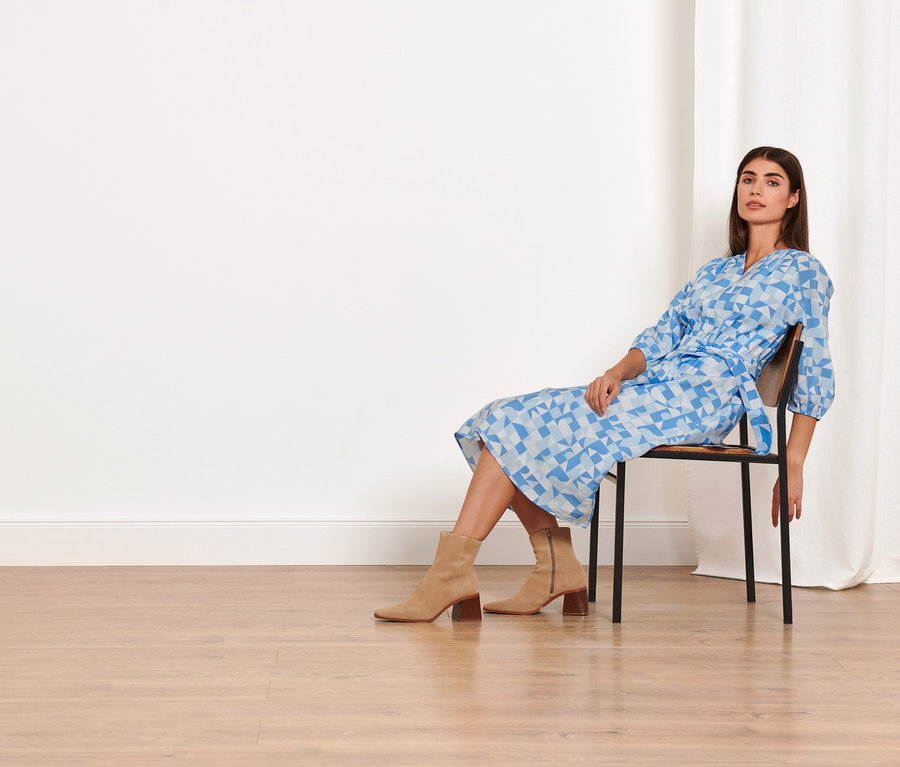 Nő ül egy széken, és mintás szövött ruhát visel.