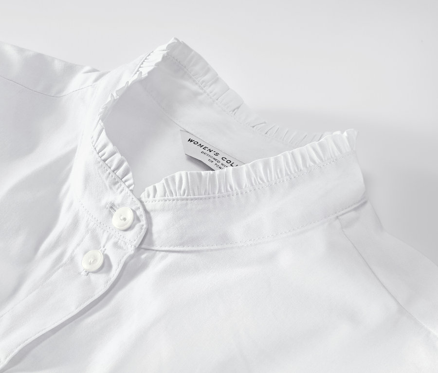 Egy fehér, fodros részletekkel díszített női blúz részlete.