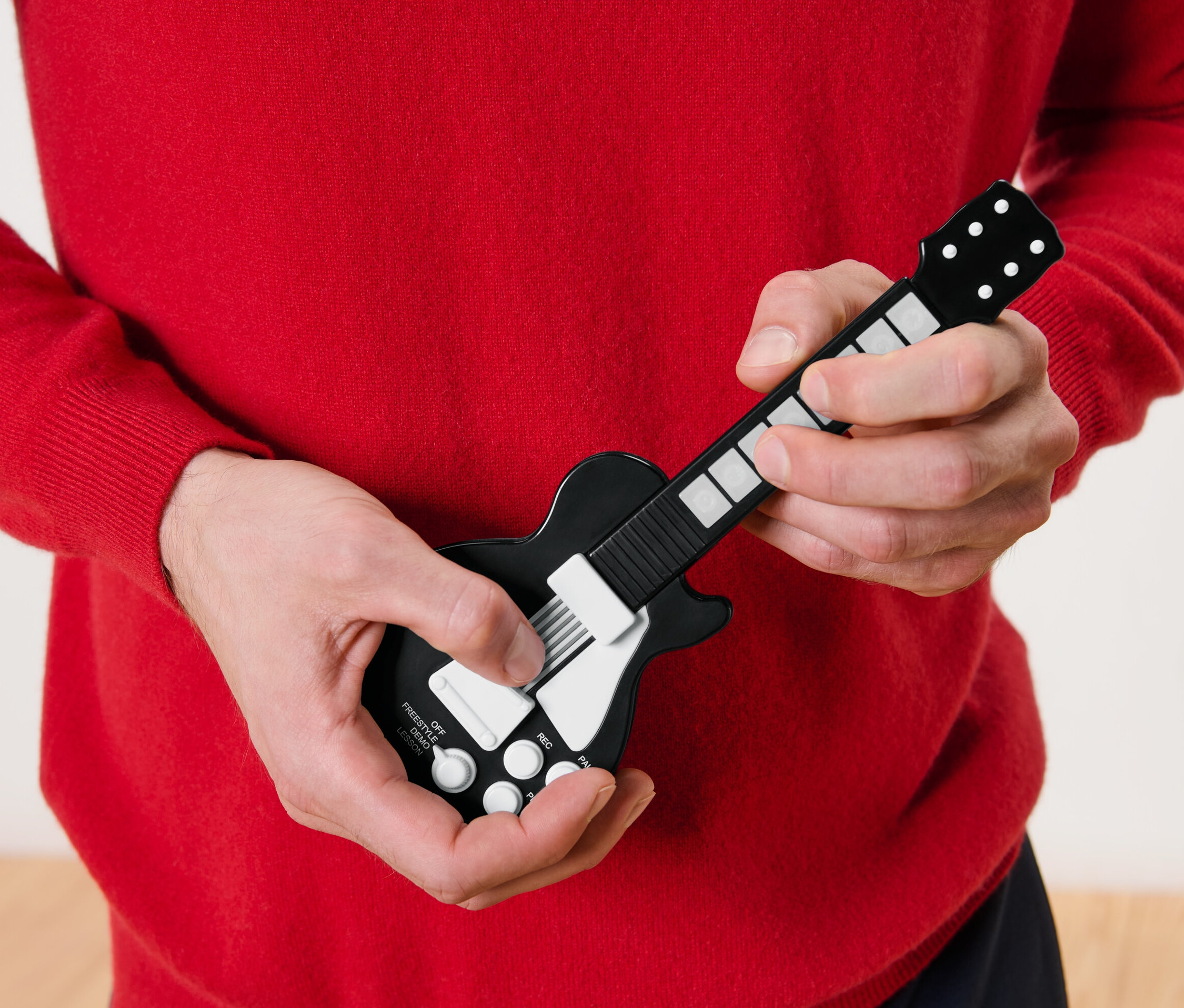 Egy piros pulóvert viselő férfi egy elemes ujjgitáron játszik.