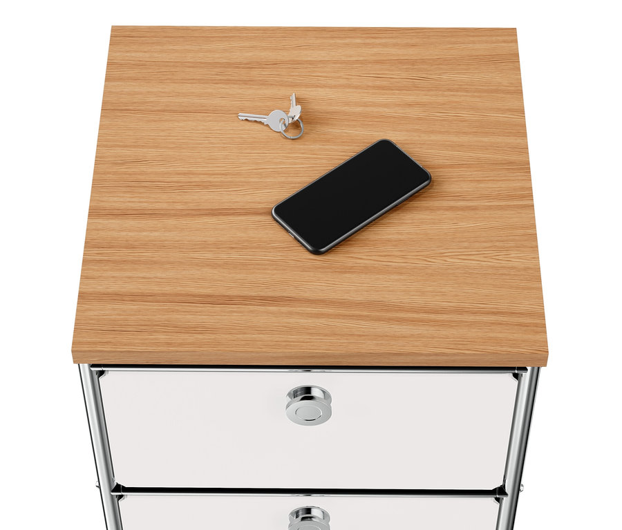 Kulcsok és mobiltelefon fekszik egy keskeny, fehér »CN3« fém komódon, fa tetőlappal és 2 fiókkal.