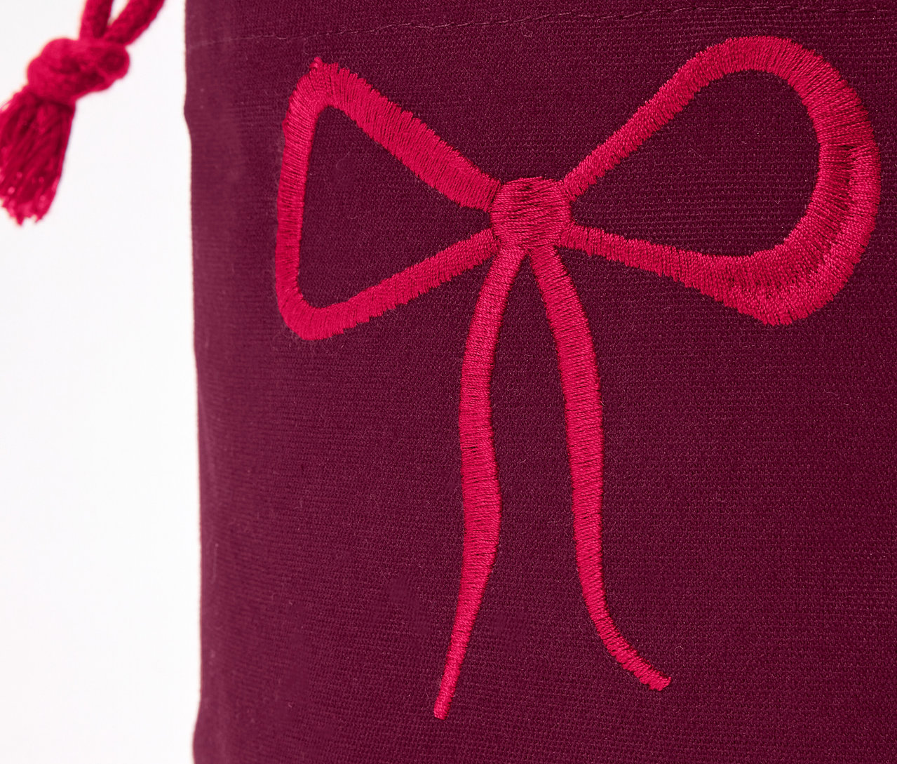 Egy bordó színű ajándéktasak részlete piros masnival.