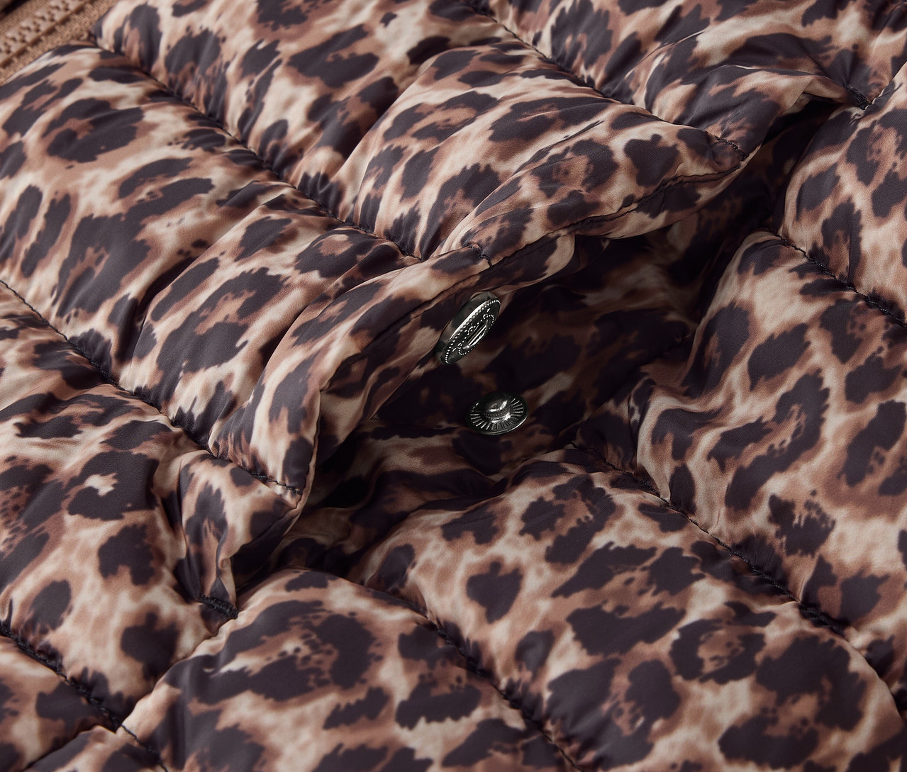 Egy barna, steppelt dzseki részlete állatmintával és ezüst patentokkal.