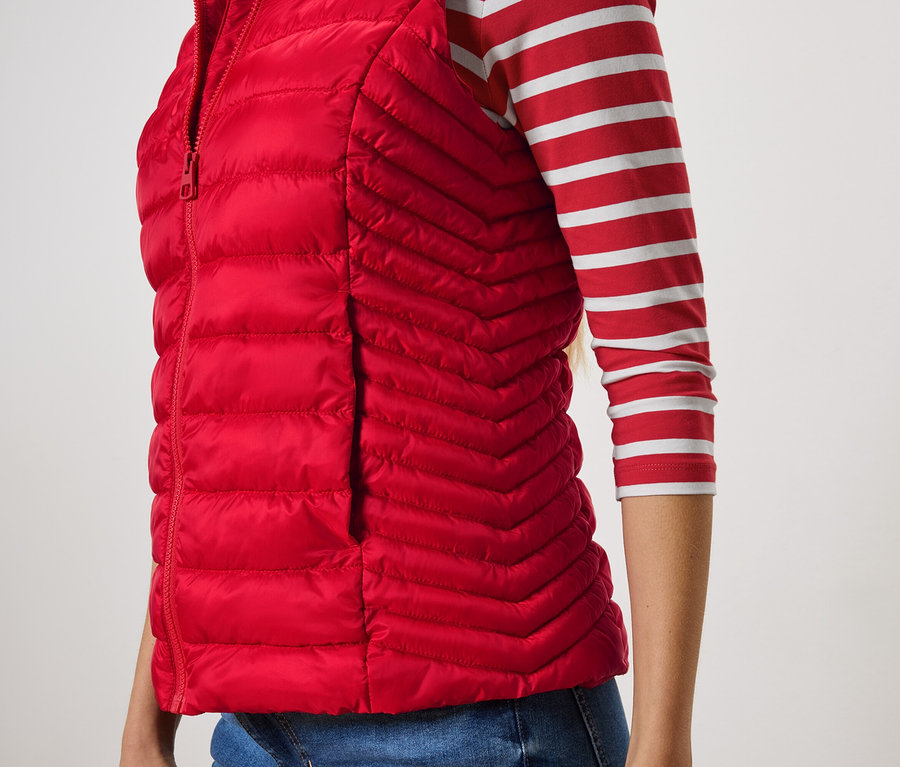 Részleges kilátás egy nőre, aki piros steppelt mellényt és csíkos pólót visel.