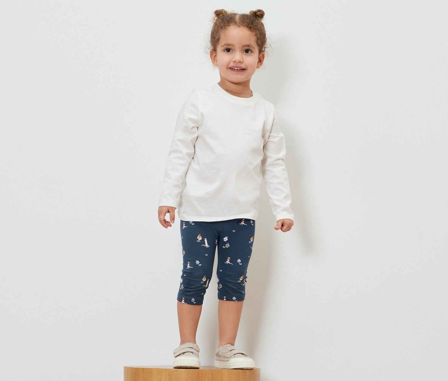 Egy lány áll egy fa talapzaton, és tengerész stílusú 3/4-es leggingset visel.