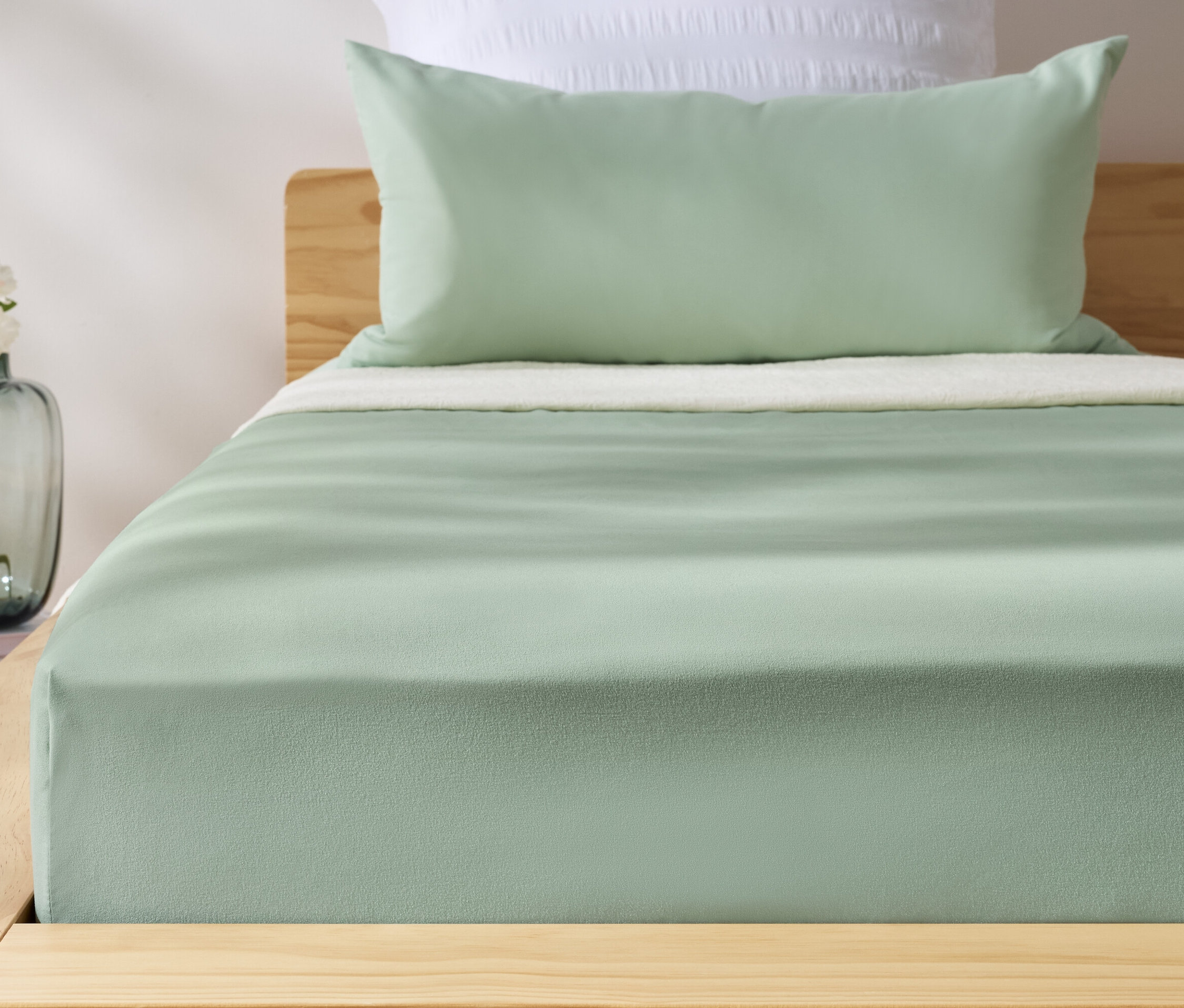 Zöld mikroszálas gumis lepedő egy ágyon. Az ágy mellett egy váza virágokkal.