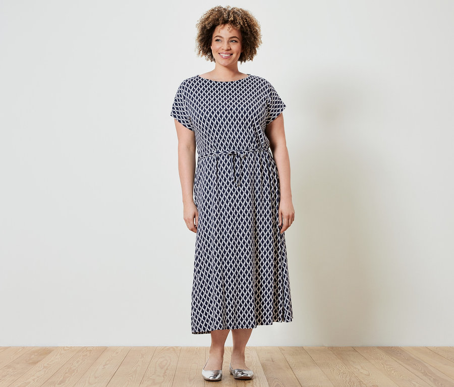 Nő áll és mintás jersey midiruhát visel.
