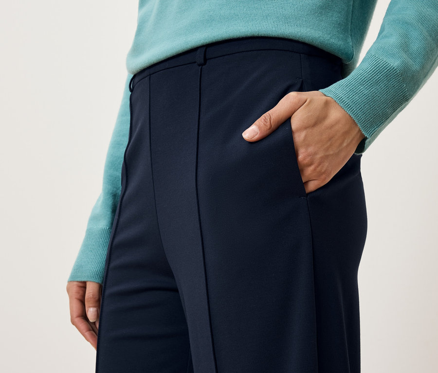 Egy nő részlete, aki kék nadrágot és pulóvert visel, és a kezét a zsebében tartja.