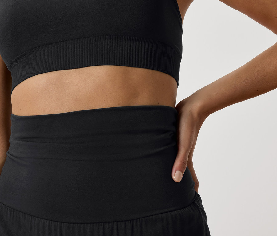 Egy nő részlete, aki fekete sportmelltartót és fekete sport rövidnadrágot visel.