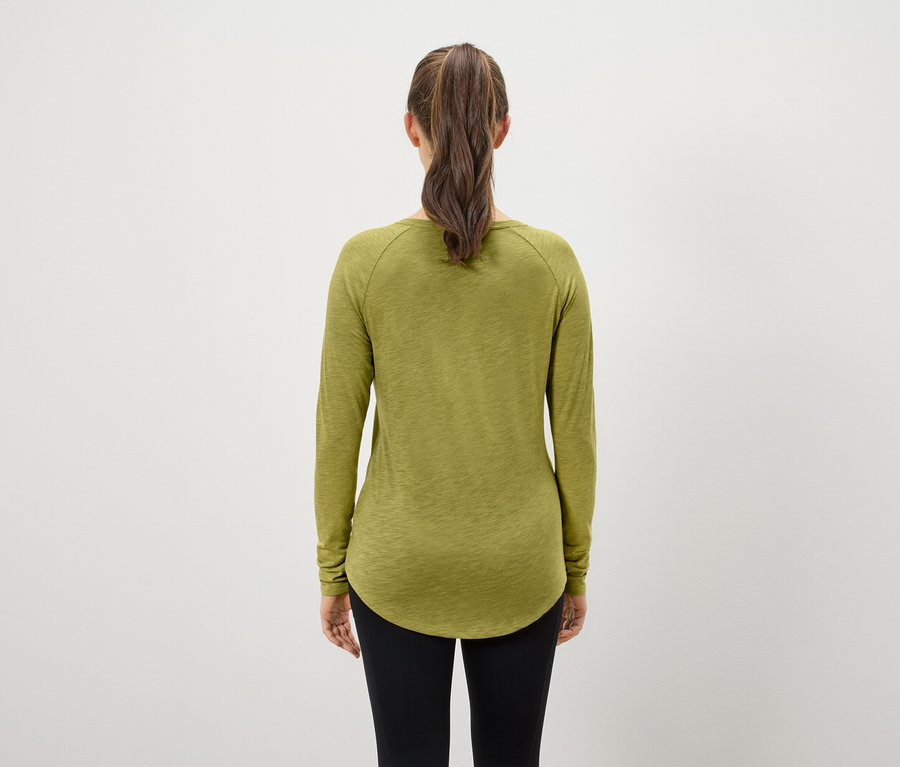 Hátulnézet egy lófarokba kötött barna hajú nőről, aki olívazöld hosszú ujjú pólót és fekete leggingst visel.