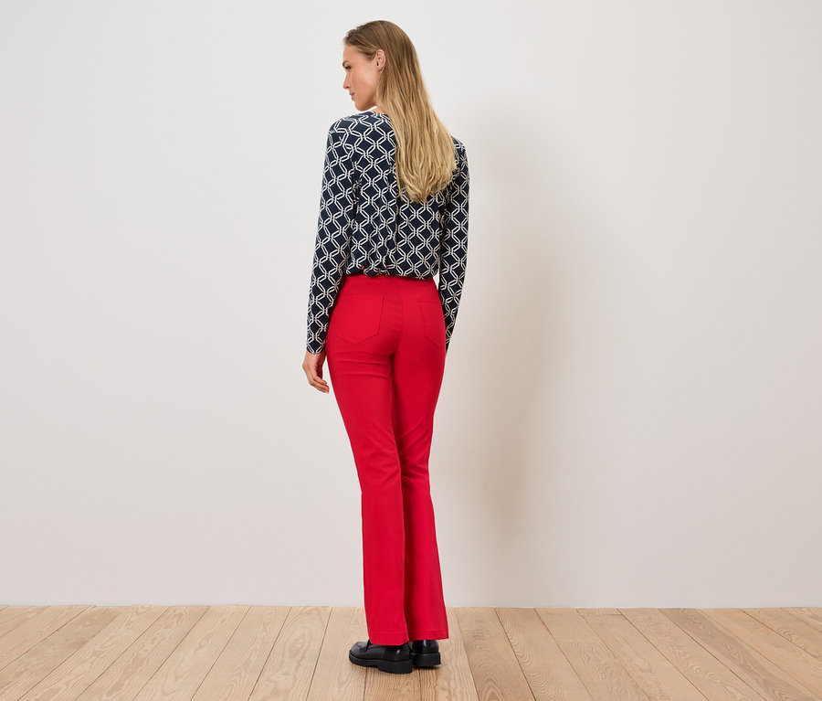 Egy nő háttal áll, mintás blúzt és piros nadrágot visel.