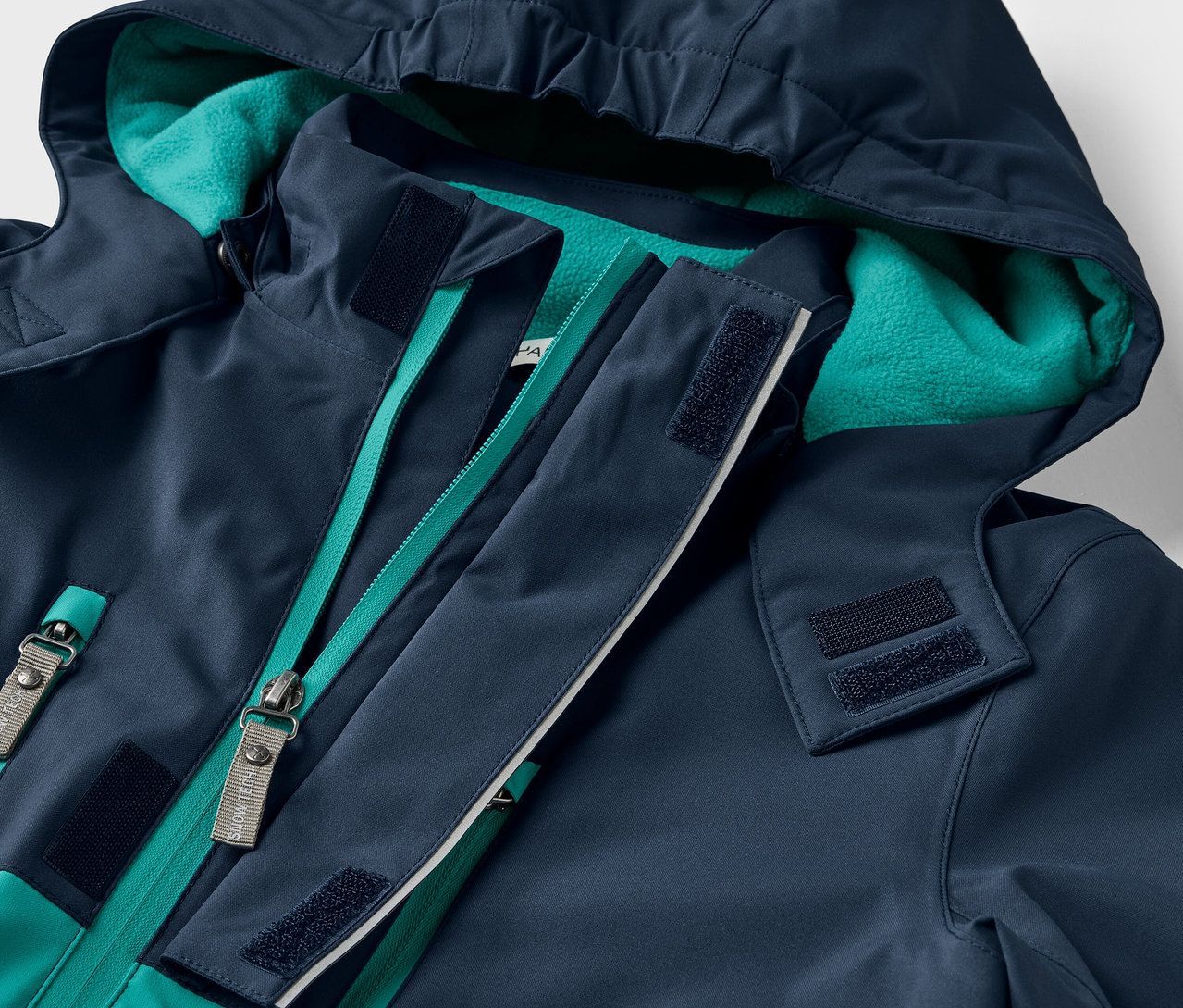 Egy sötétkék, kapucnis kabát részlete zöld cipzárral.