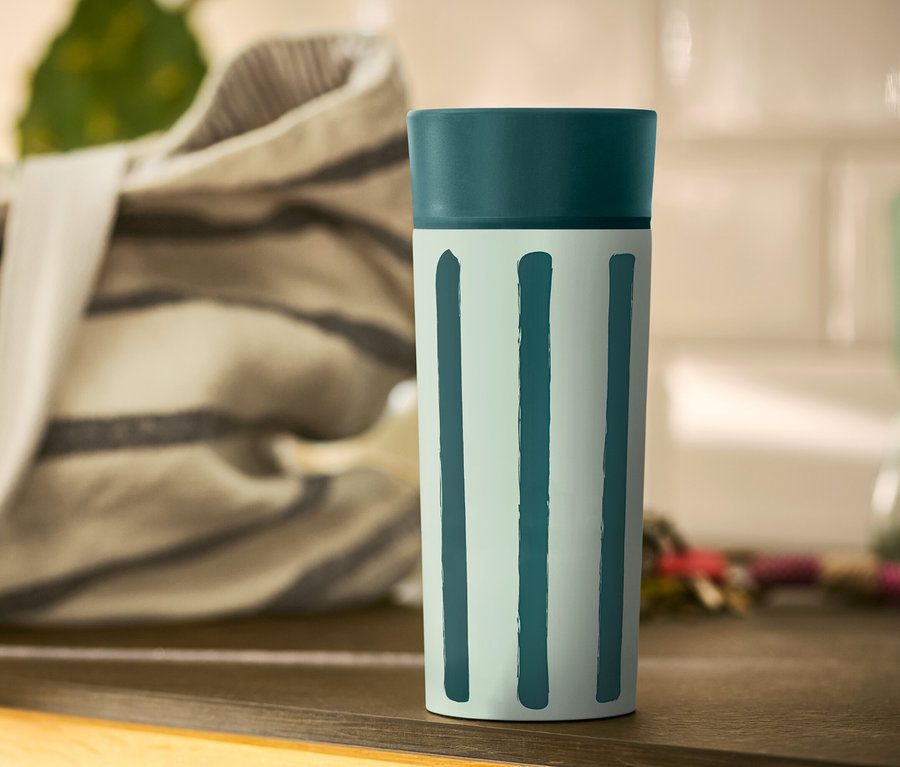 Egy csíkos Coffee-to-go bögre áll az asztalon.