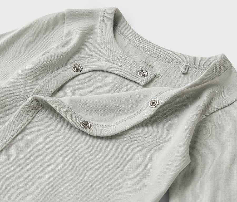 Egy világoskék-szürke, hosszú ujjú, patentos babaruha közeli képe.