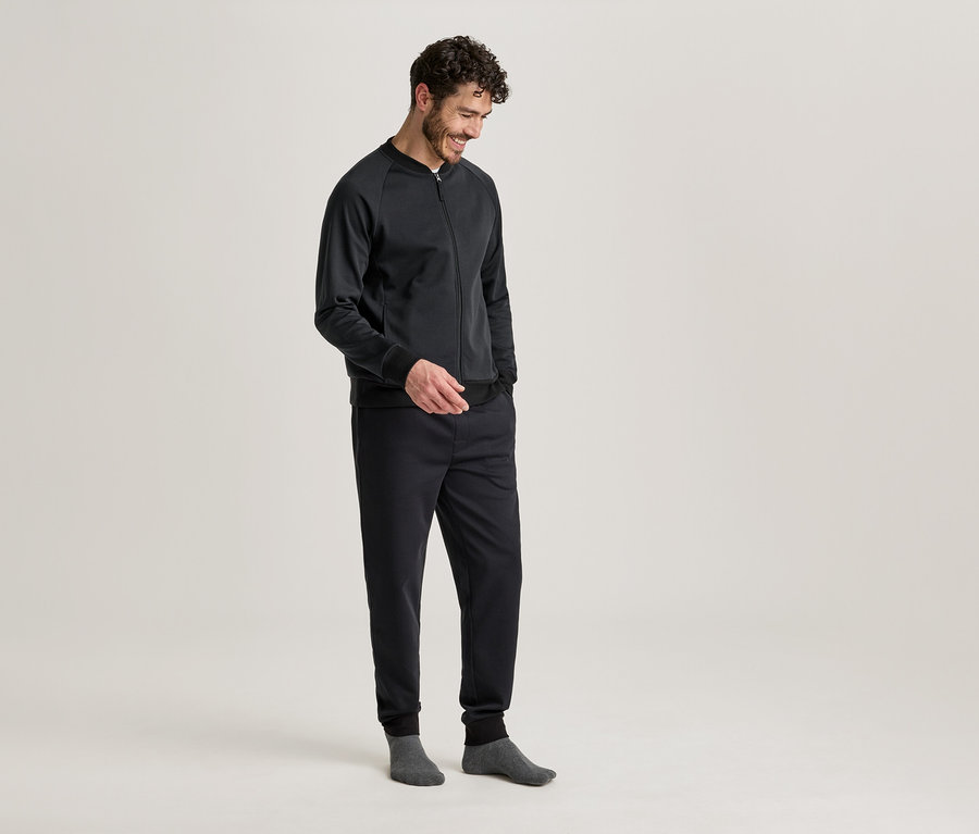 Férfi sötét kabátban és nadrágban, kezével a zsebében, szürke zokniban.