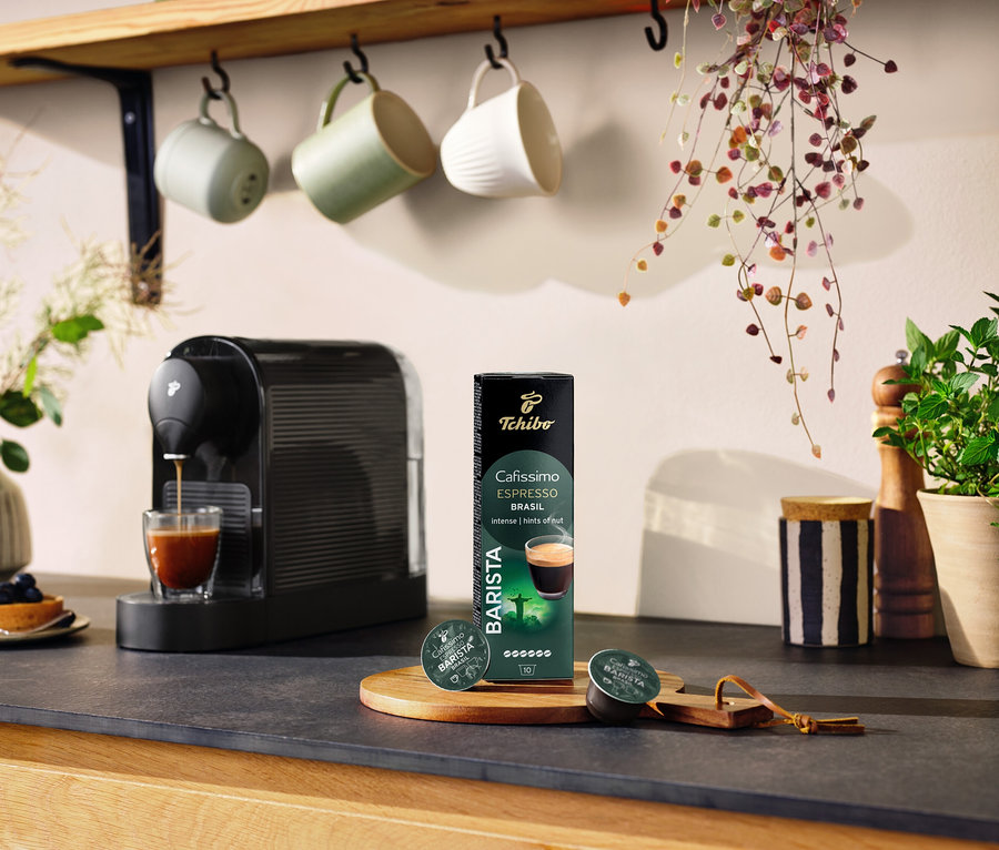 Fekete kávéfőző készít kávét egy pohárba az Espresso Brasil - 10 db kávékapszula csomagolása mellett.