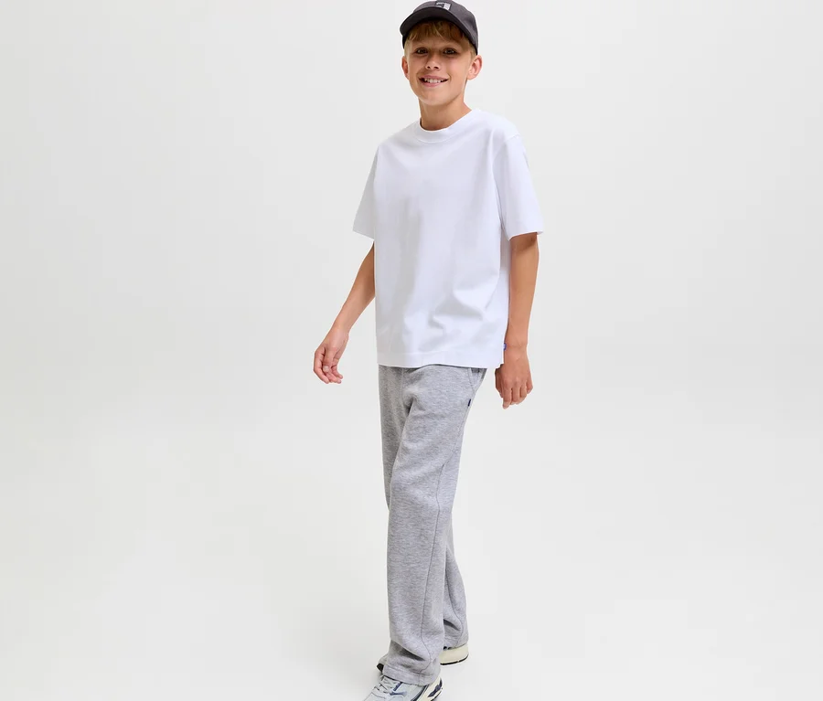 Mosolygó fiú fehér pólóban, sötét baseball sapkában és szürke Jack&Jones Bradley szabadidőnadrágban.