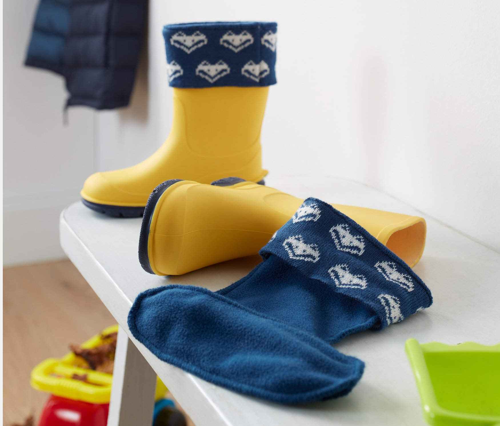 Sárga gumicsizma Kisgyerek gumicsizma béléssel egy fehér padon.
