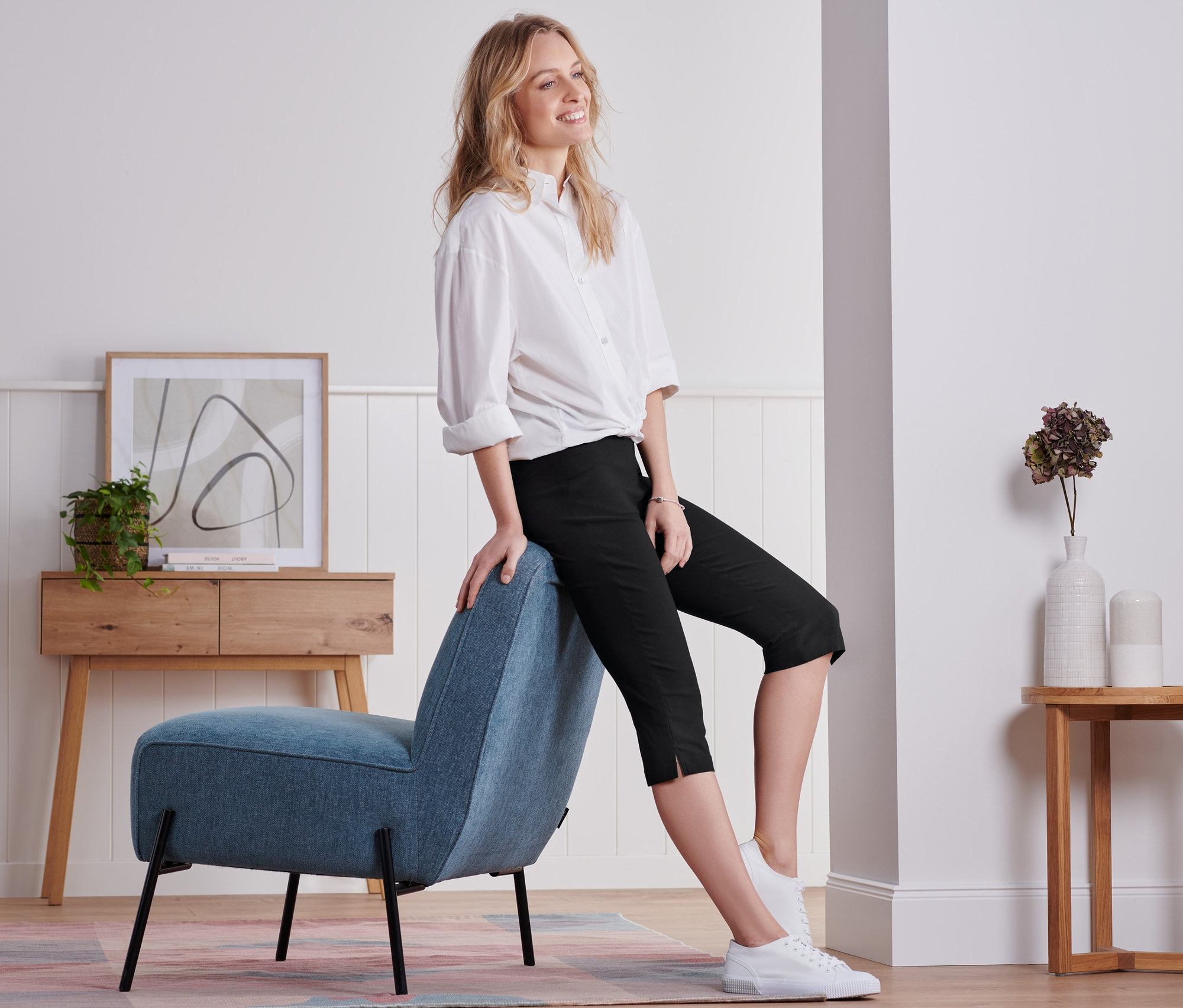 Nő ül egy kék széken, fekete, háromnegyedes bengalin nadrágot visel.