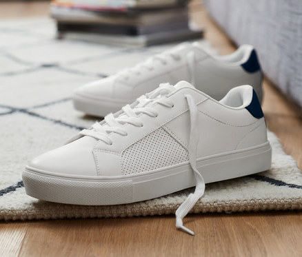 Két sneaker cipő van a padlón egy szürke kanapé mellett.