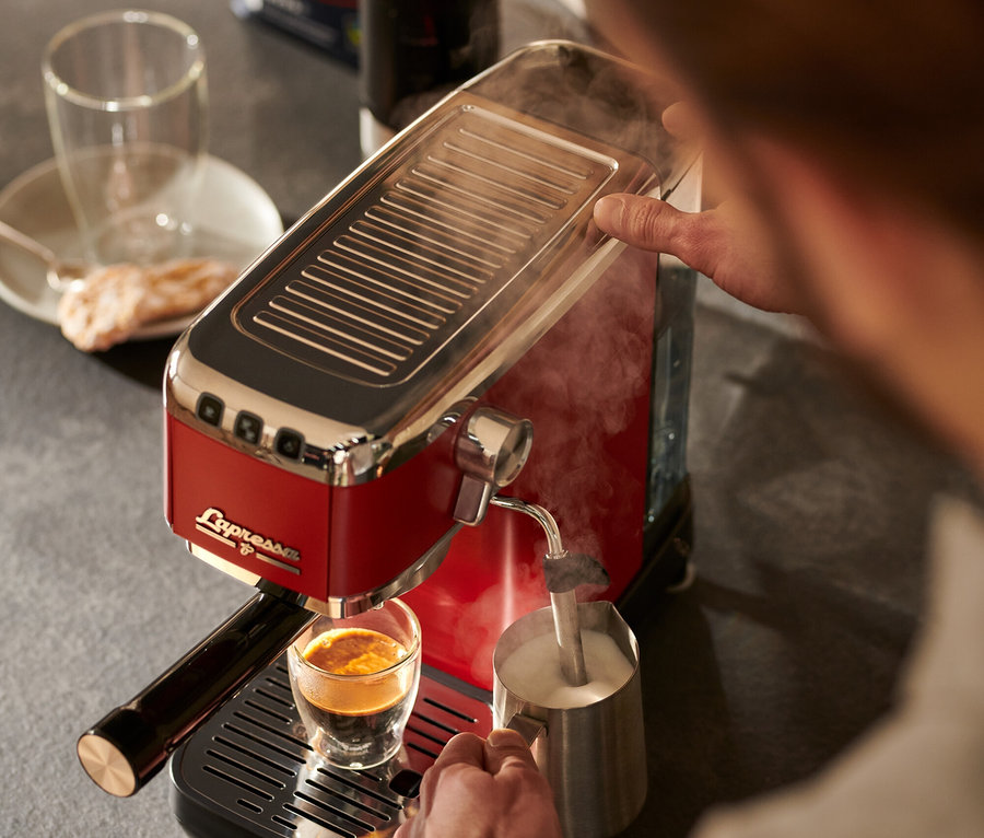 Egy férfi kávét készít és tejet habosít egy piros »Lapressa« karos eszpresszó kávéfőzővel.