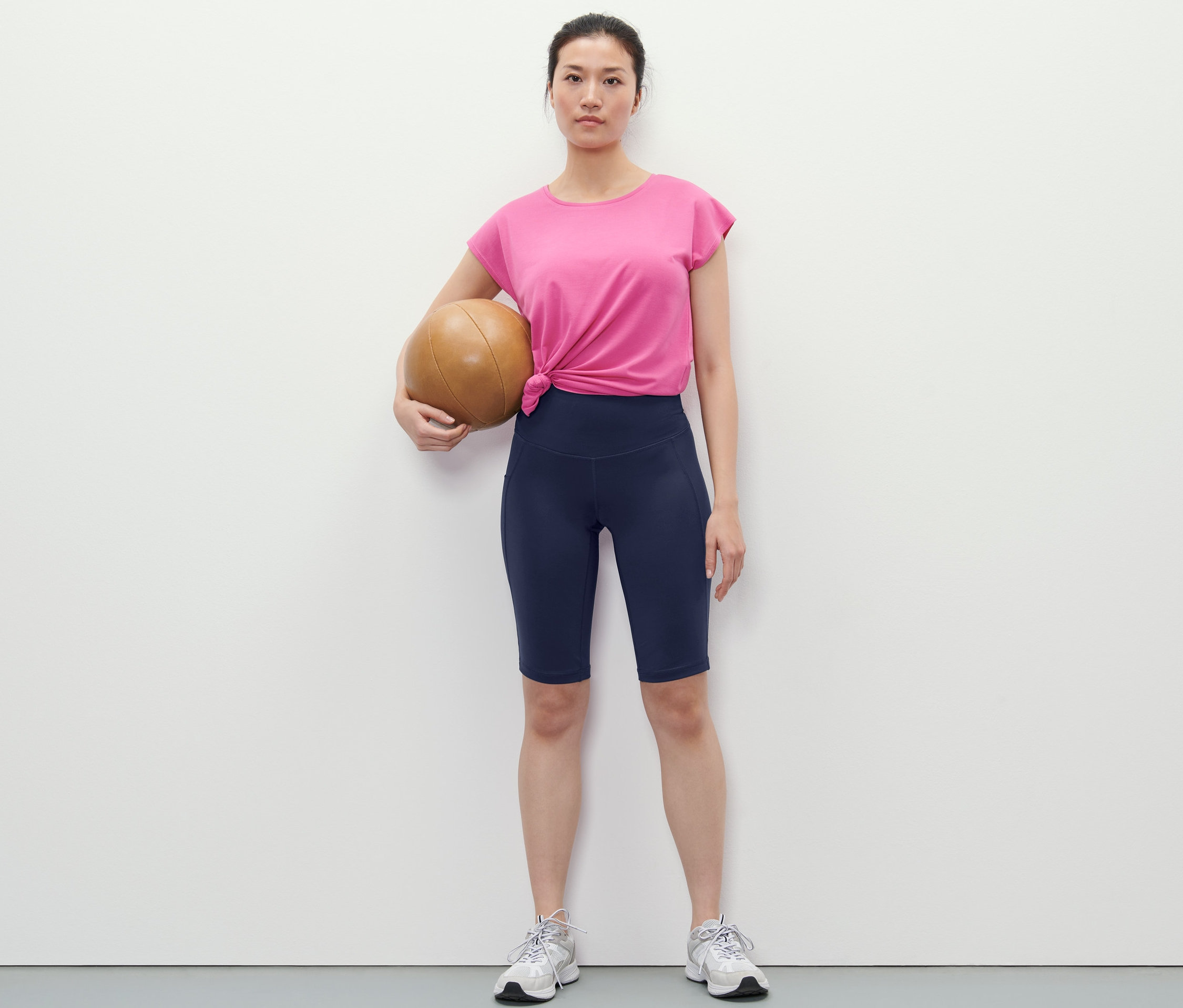 Nő kosárlabdát tart és sötétkék sport rövidnadrágot visel.