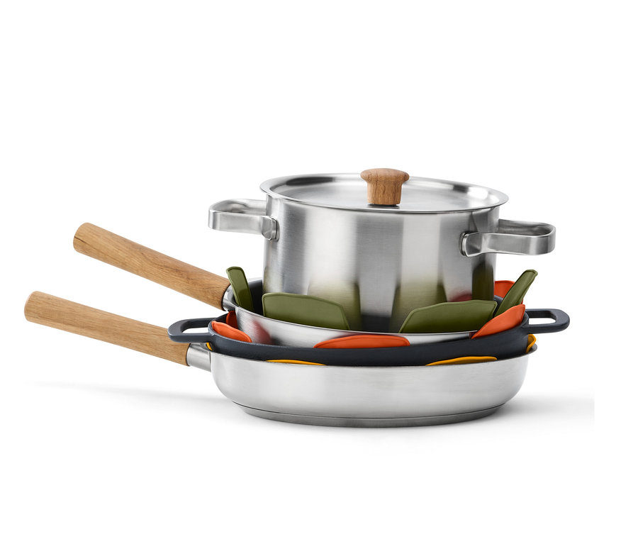 Egy rozsdamentes acélból készült fedős edény és serpenyők egymásra vannak rakva, köztük 3 db szilikon edényvédővel.