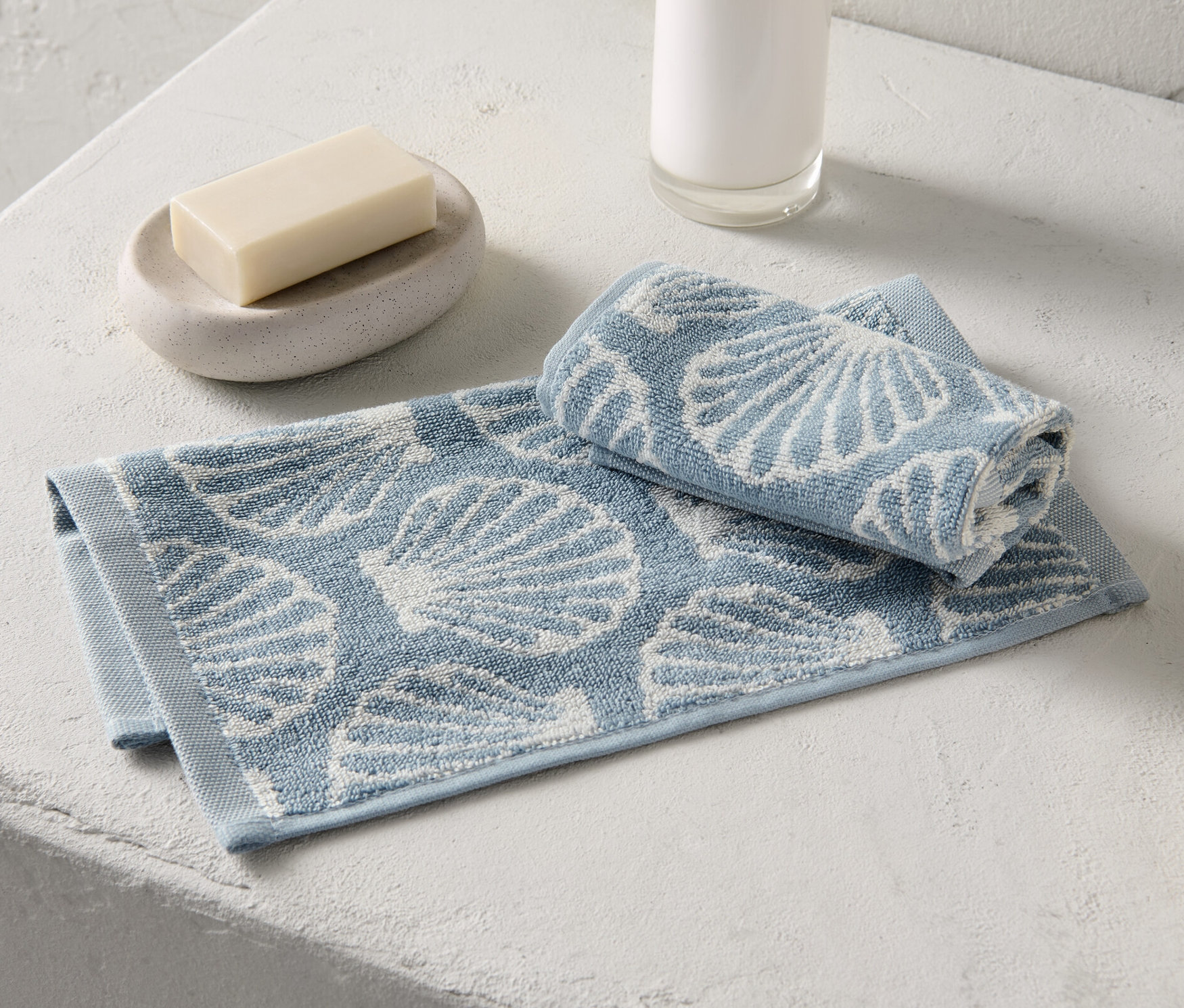 Két kagylómintás vendégtörölköző fekszik szappan és szappanadagoló mellett.