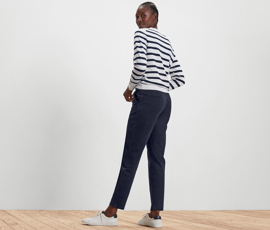 Nő pózol sötétkék chino nadrágban és csíkos pulóverben.