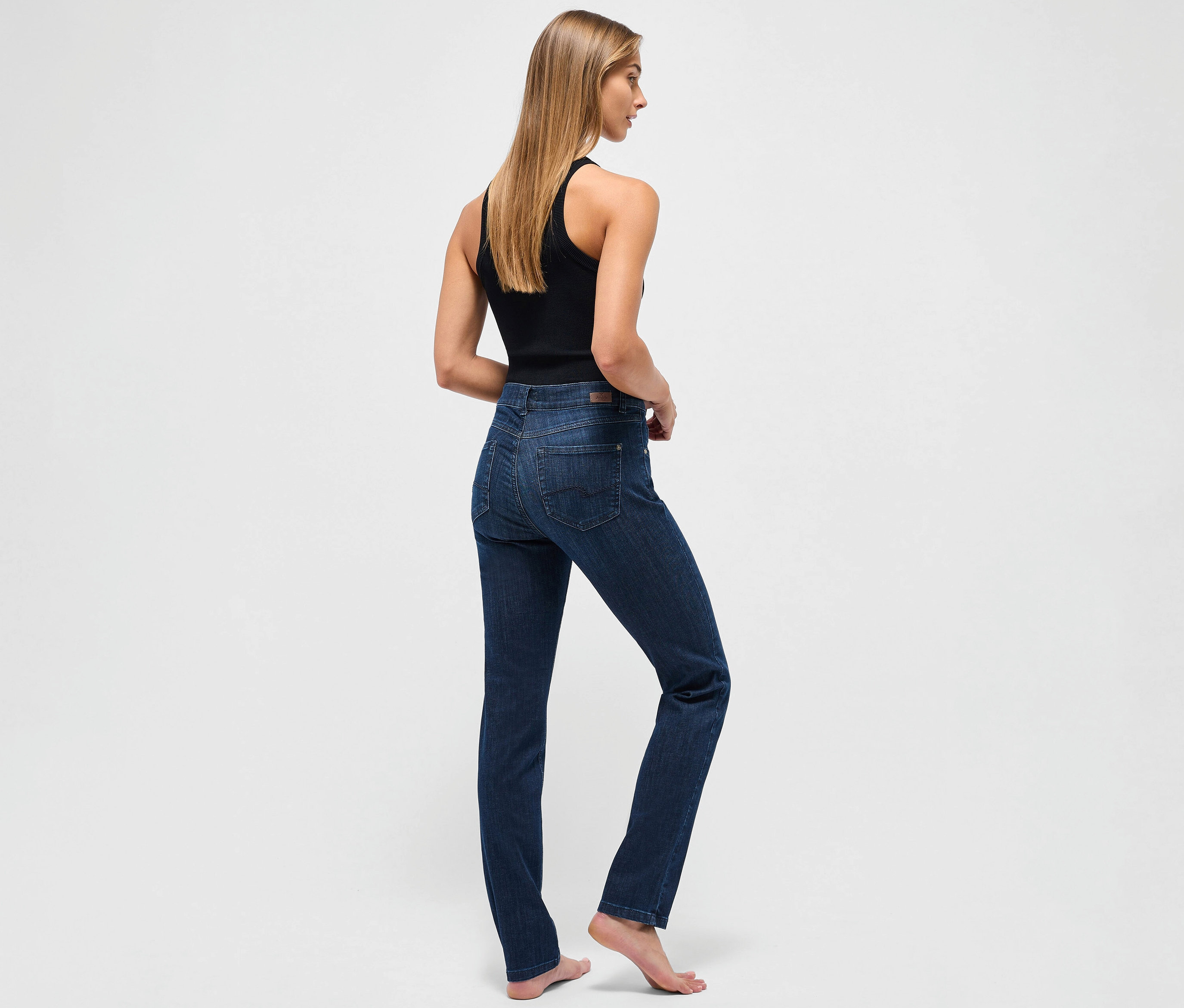 Egy nő háttal áll a kamerának, sötétkék Angels »Cici« slim fit farmert és fekete trikót visel.