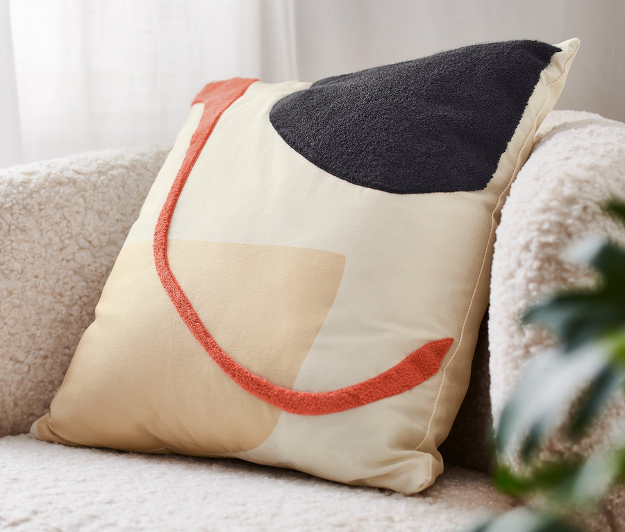 Egy absztrakt mintás díszpárna töltettel fekszik egy széken.