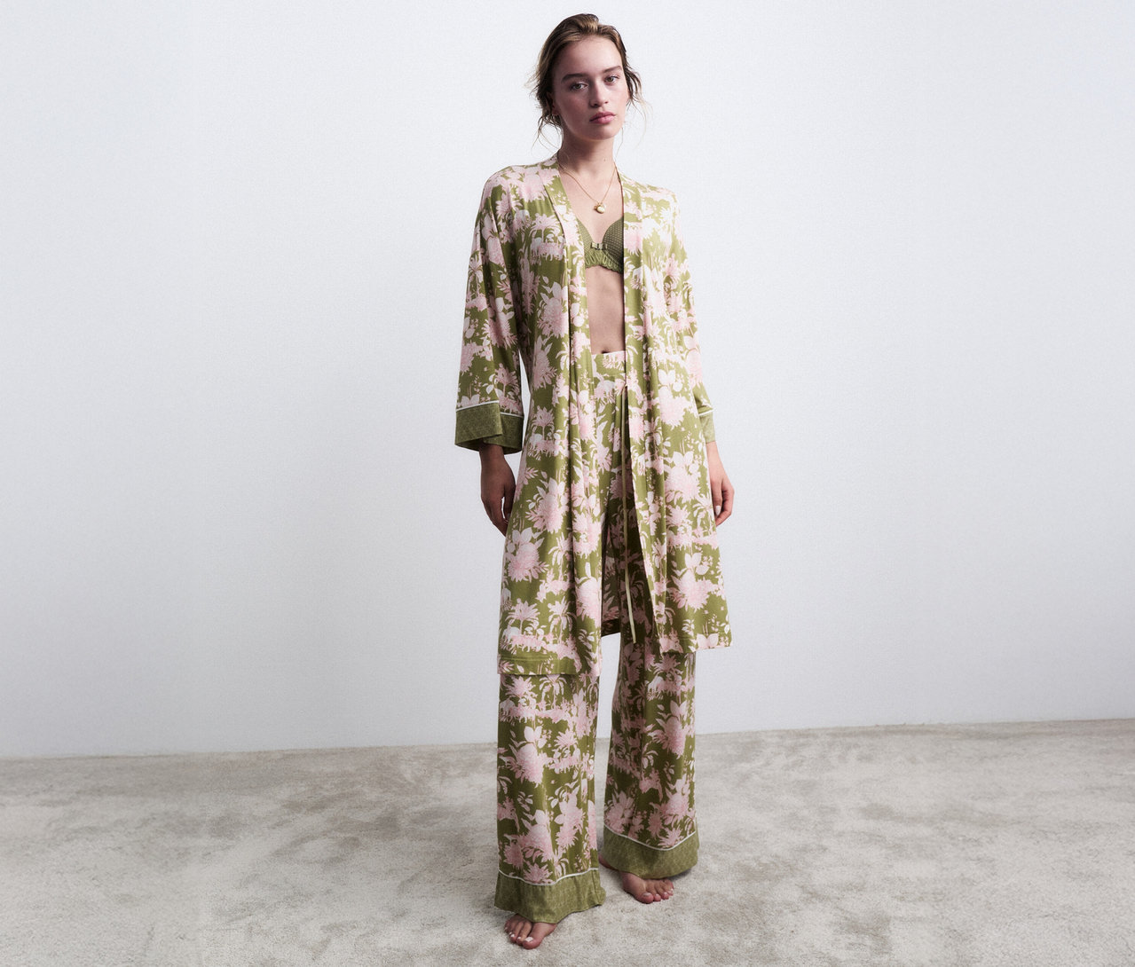 Nő áll mezítláb zöld, virágmintás pizsamában hozzáillő köntössel.
