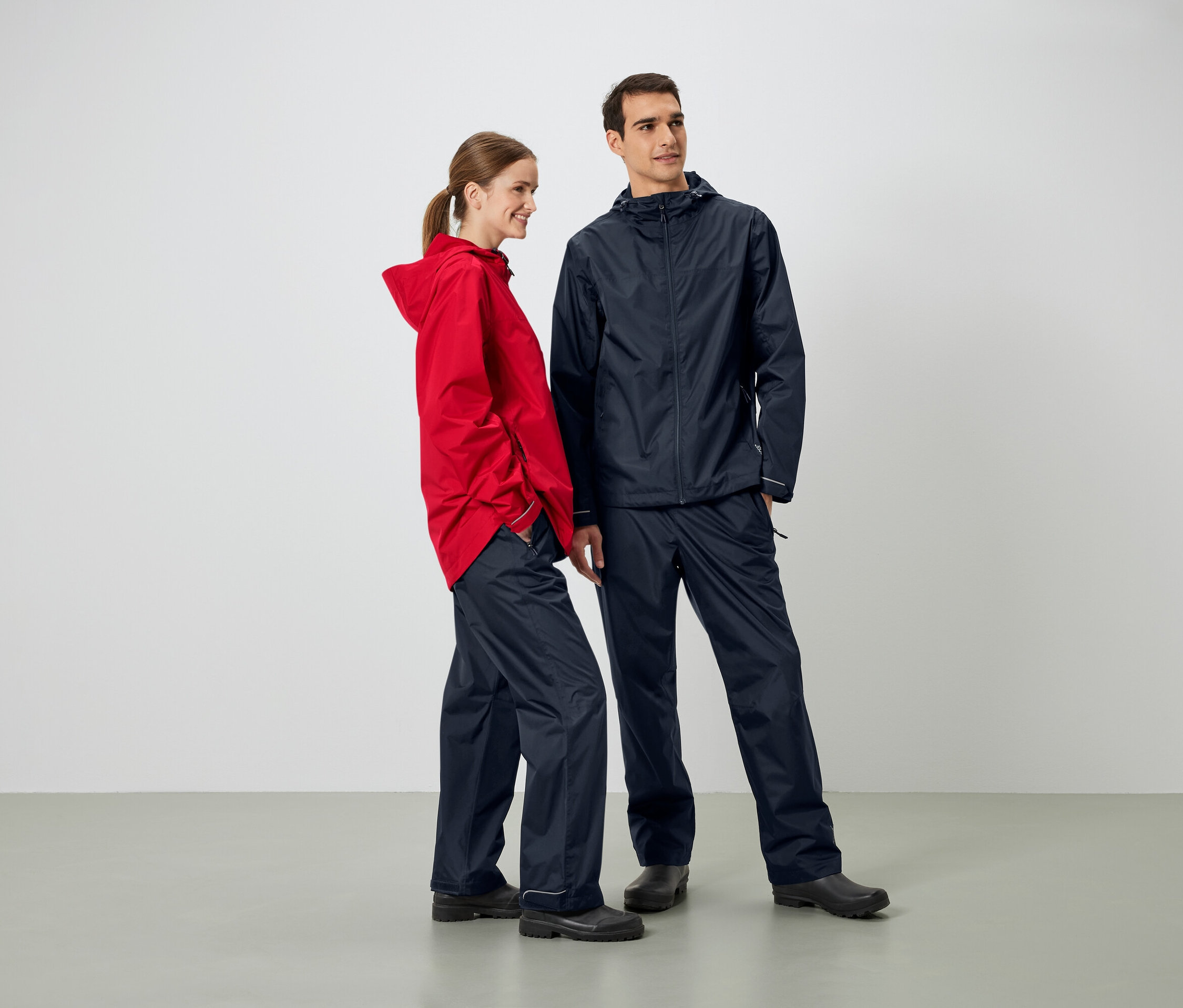 Egy férfi és egy nő egymás mellett állnak, esőkabátot és esőnadrágot viselnek.