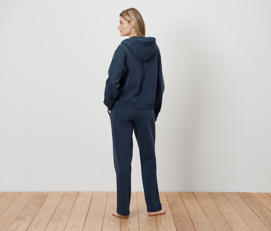 Egy nő háttal áll, sötétkék kapucnis pulóvert és melegítőalsót visel.