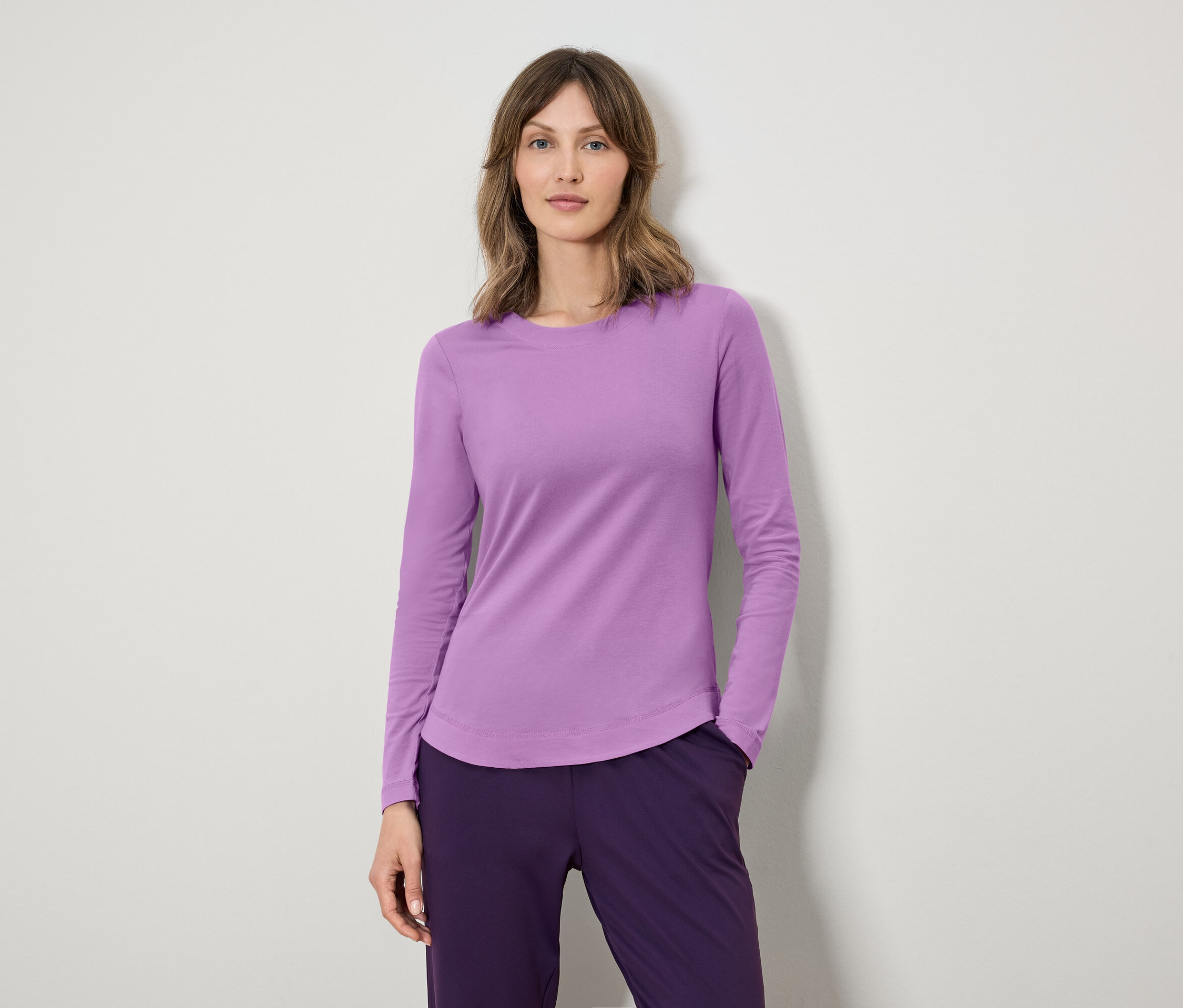 Nő lila, hosszú ujjú pólót és sötétlila nadrágot visel.