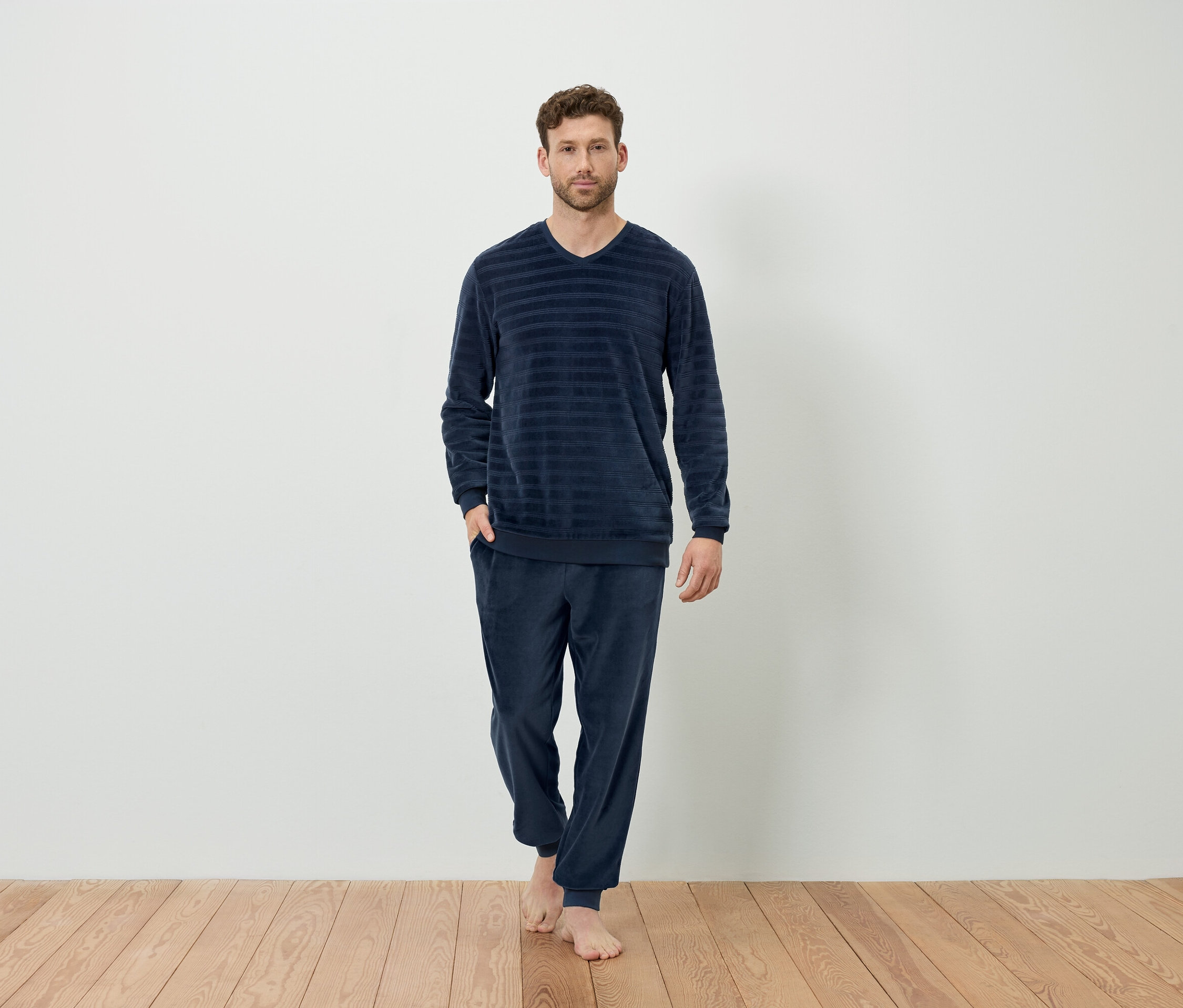 Egy férfi áll mezítláb, sötétkék, csíkos pizsamában.
