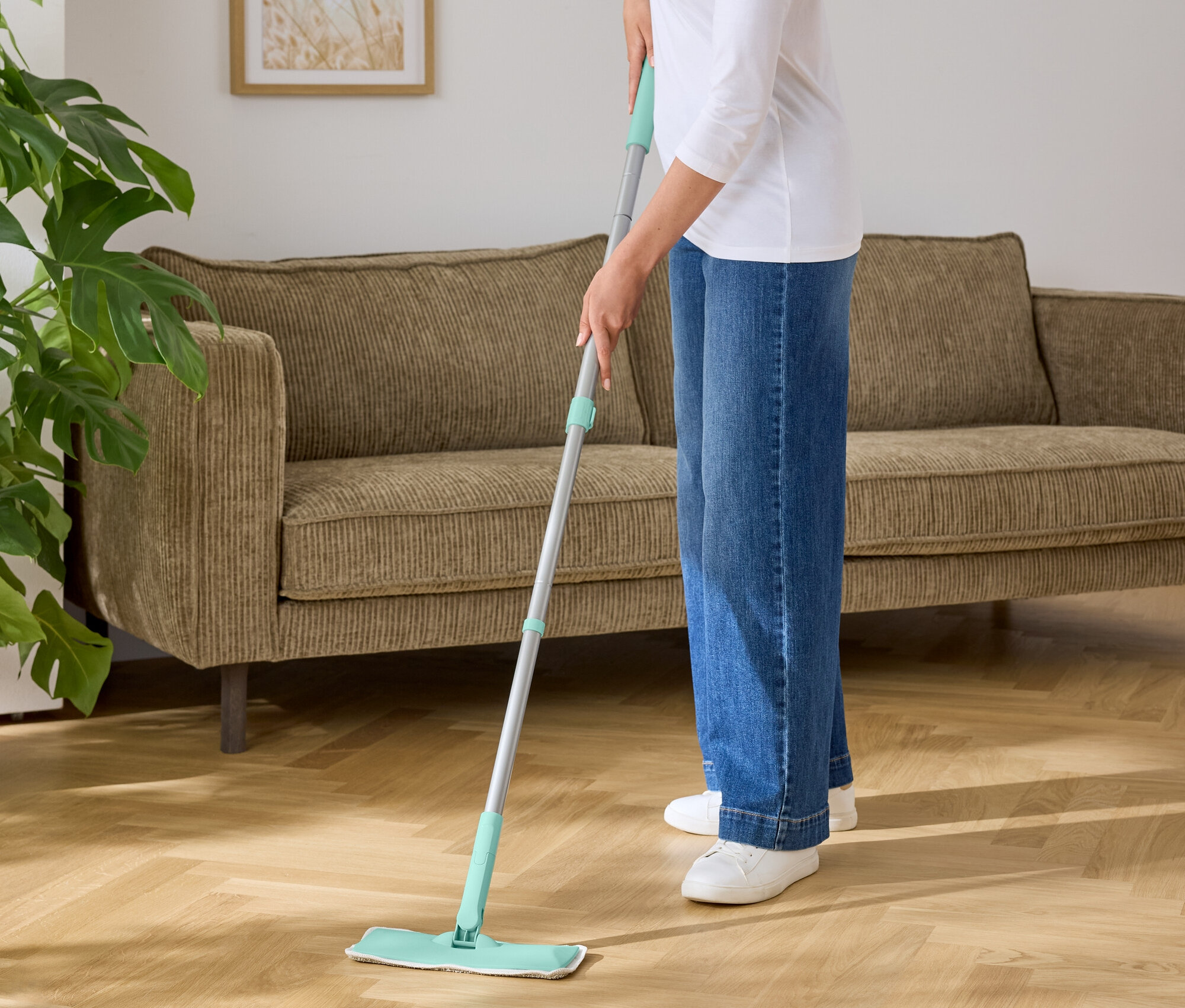 Nő töröl fel egy fapadlót egy türkizkék aljú felmosóval.