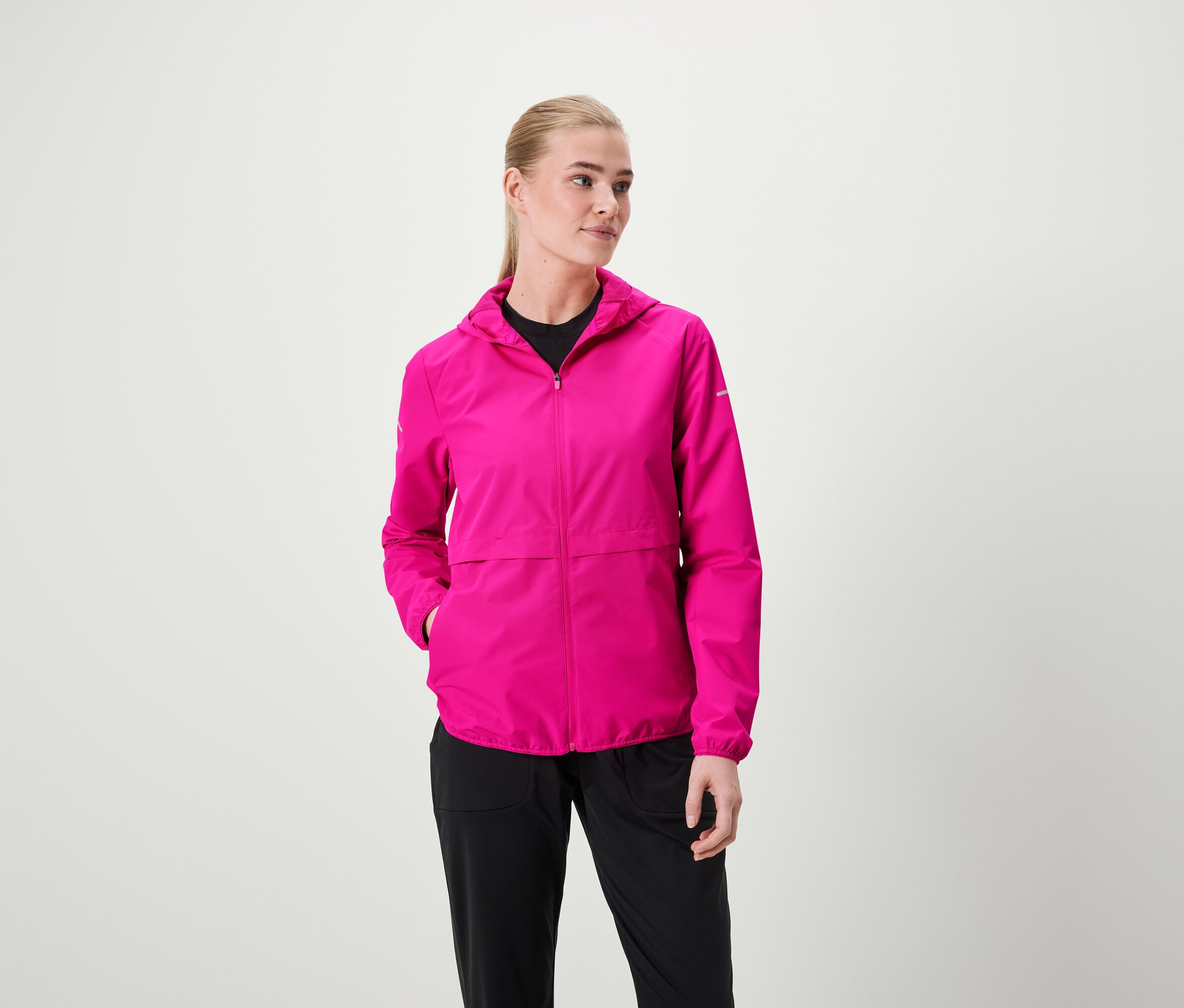 Nő visel rózsaszín kapucnis kabátot és fekete nadrágot.