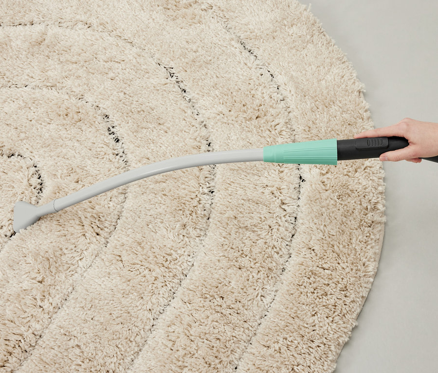 Egy személy porszívófejjel porszívóz egy kerek szőnyeget.
