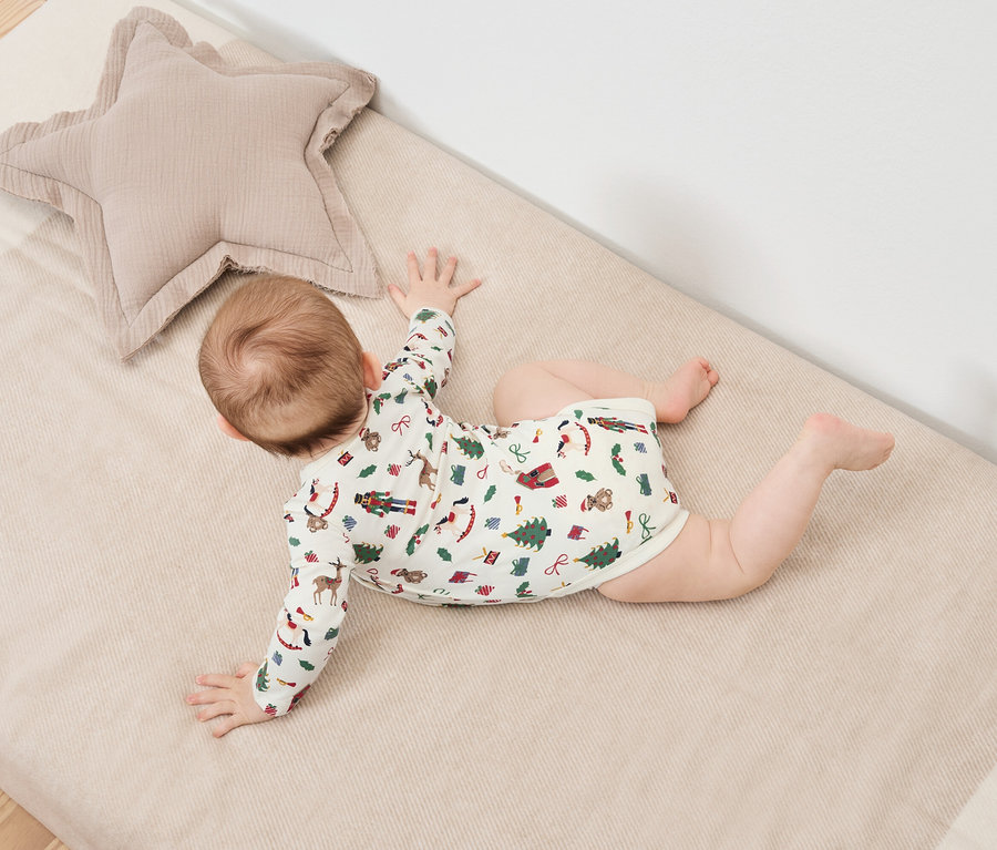 Egy baba hason fekszik egy karácsonyi mintás takarón egy bézs csillag alakú párna mellett.