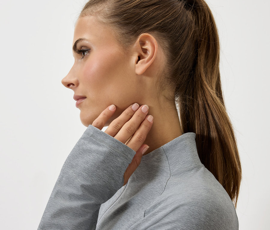 Egy barna hajú, lófarokba kötött nő profilja, aki szürke pulóverben a nyakát érinti.