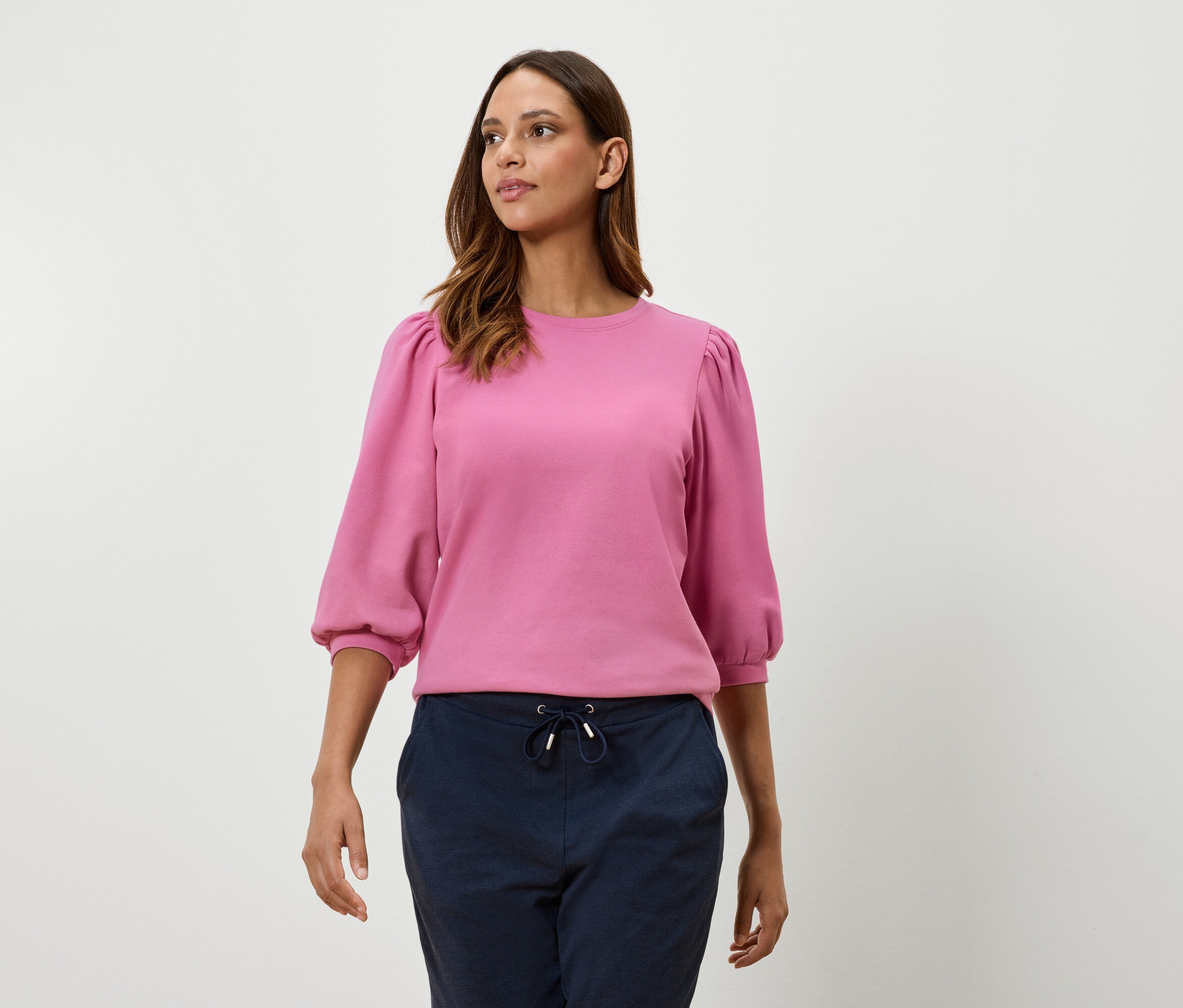 Nő rózsaszín, háromnegyedes ballonujjú pulóvert és tengerészkék nadrágot visel.