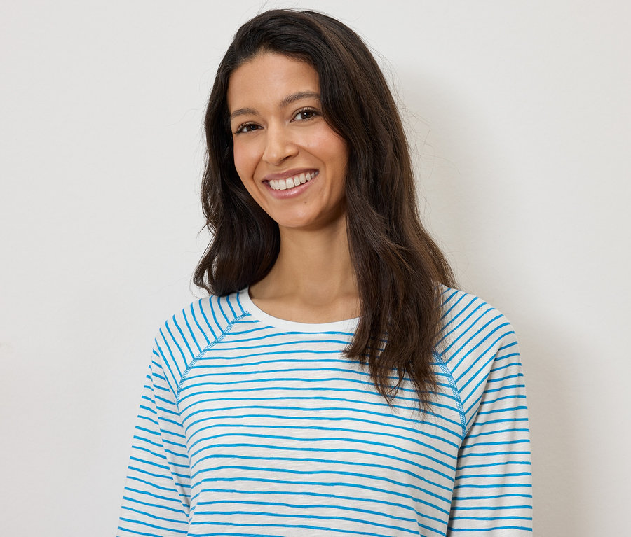 Mosolygó nő kék-fehér csíkos, hosszú ujjú felsőben, fehér háttér előtt.