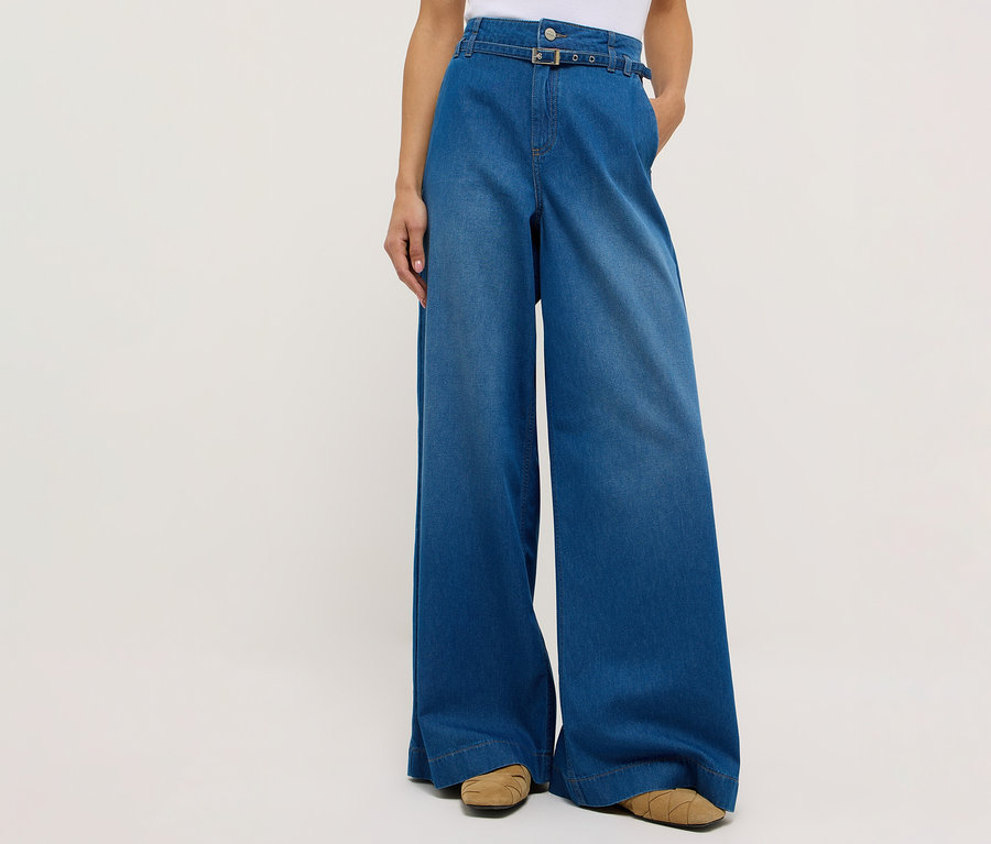 Egy személy Angels denim »Liva« letisztult, bőszárú farmert és barna cipőt visel fehér háttér előtt.
